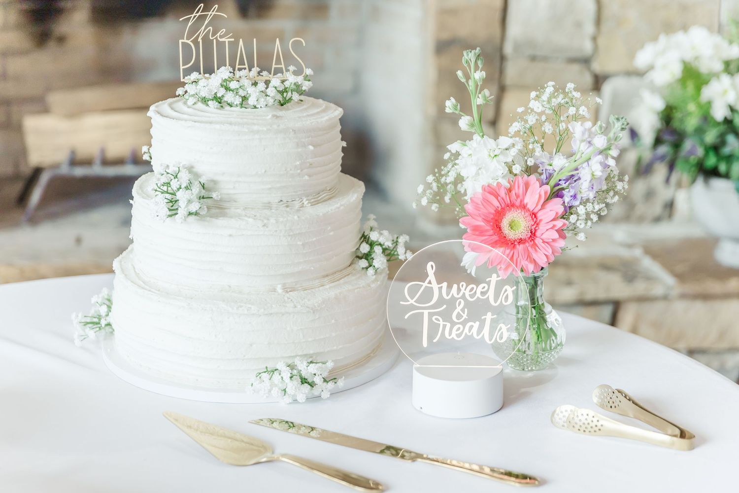 Elegant white three-tier wedding cake decorated with baby's breath flowers and a coral gerbera daisy on display.