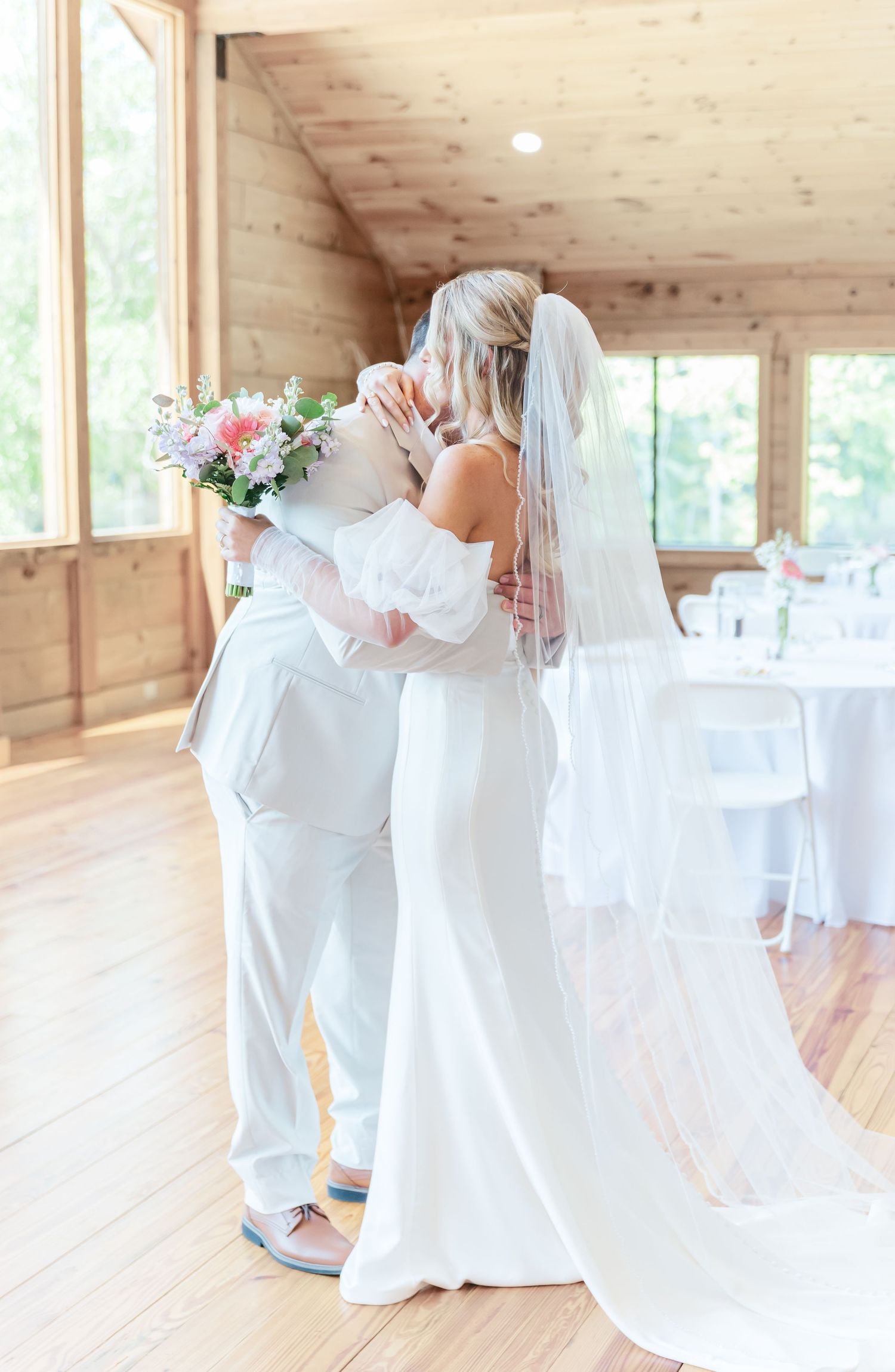 A tender embrace between newlyweds in a rustic wooden venue with natural light.