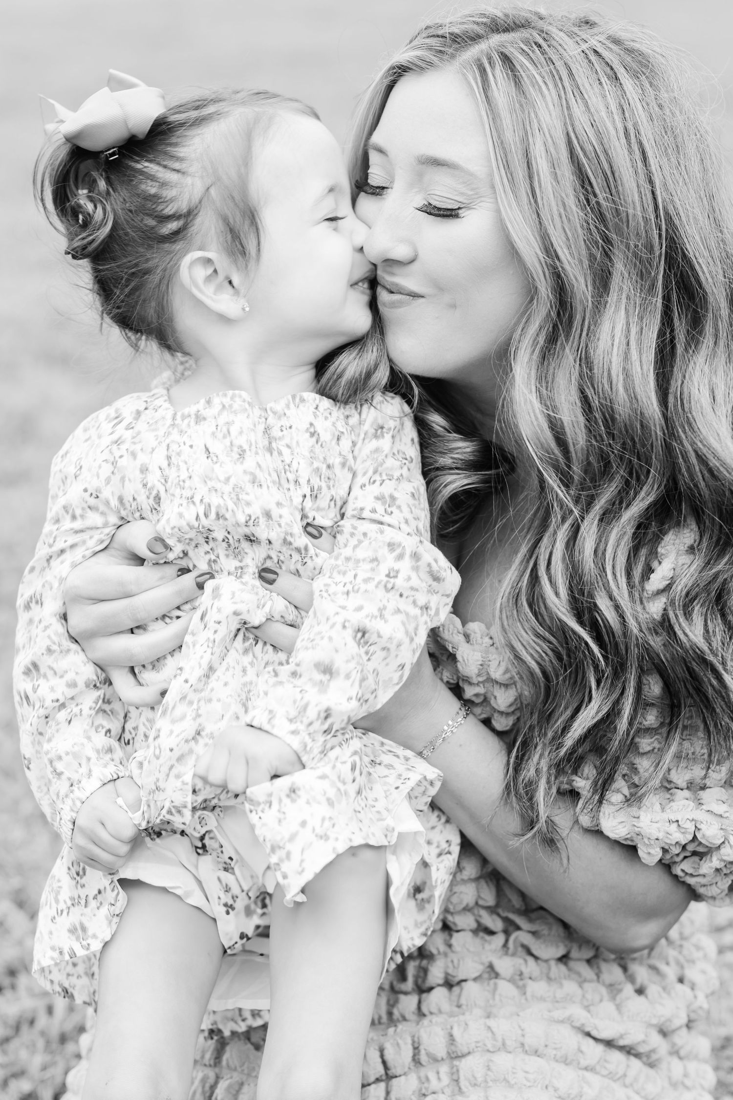 A tender black and white portrait of a mother and young daughter in matching floral dresses sharing an intimate moment.