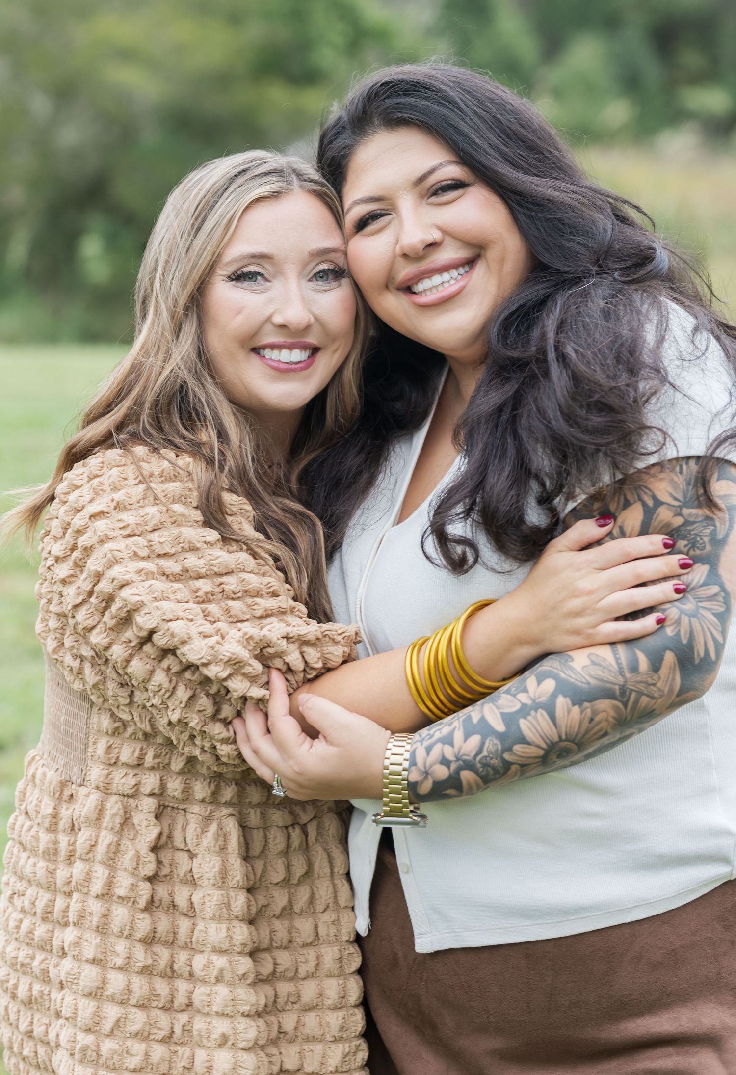 Two women embracing and laughing together while wearing casual outfits outdoors.