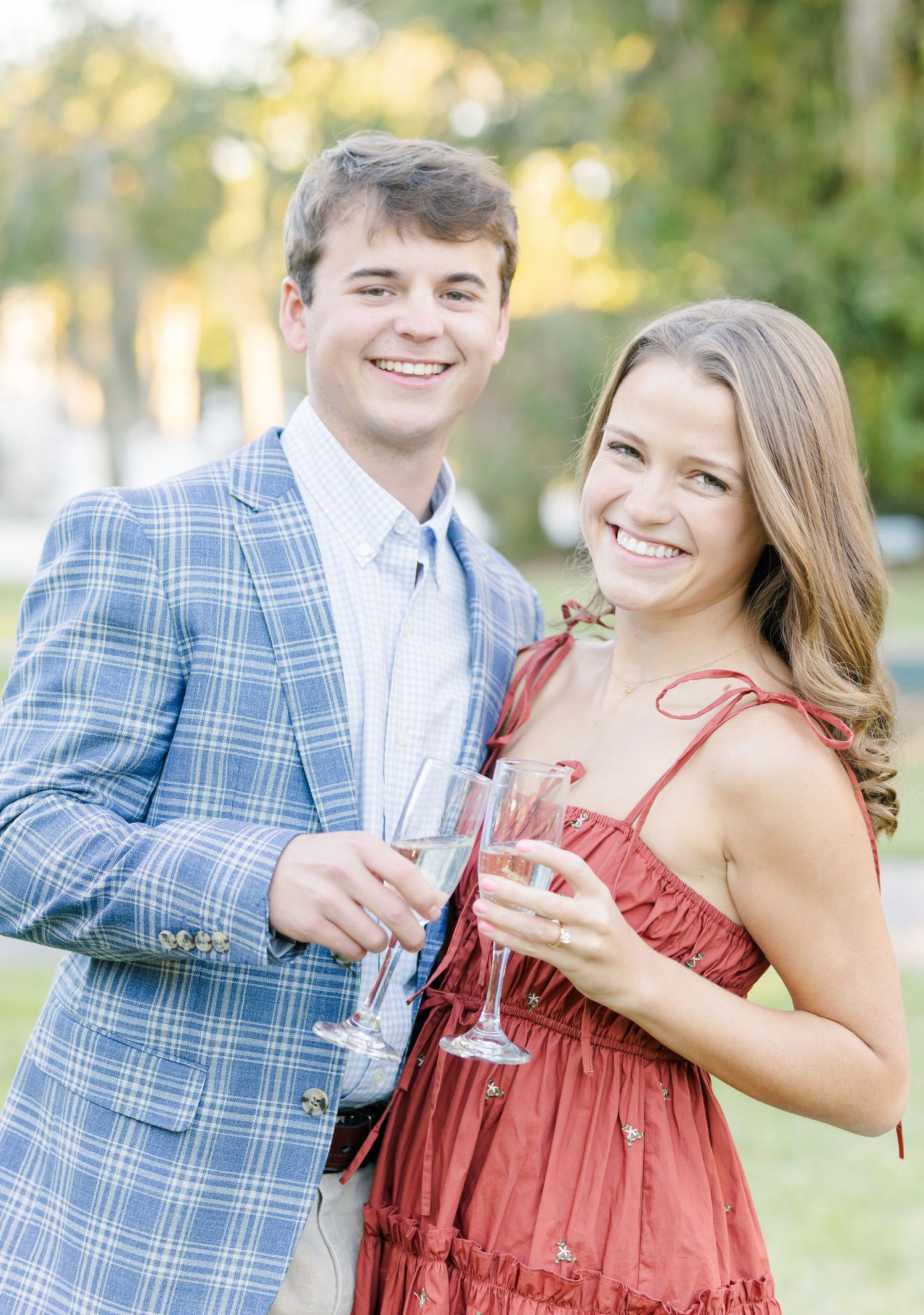 A couple laughs while holding champagne glasses during an outdoor celebration.
