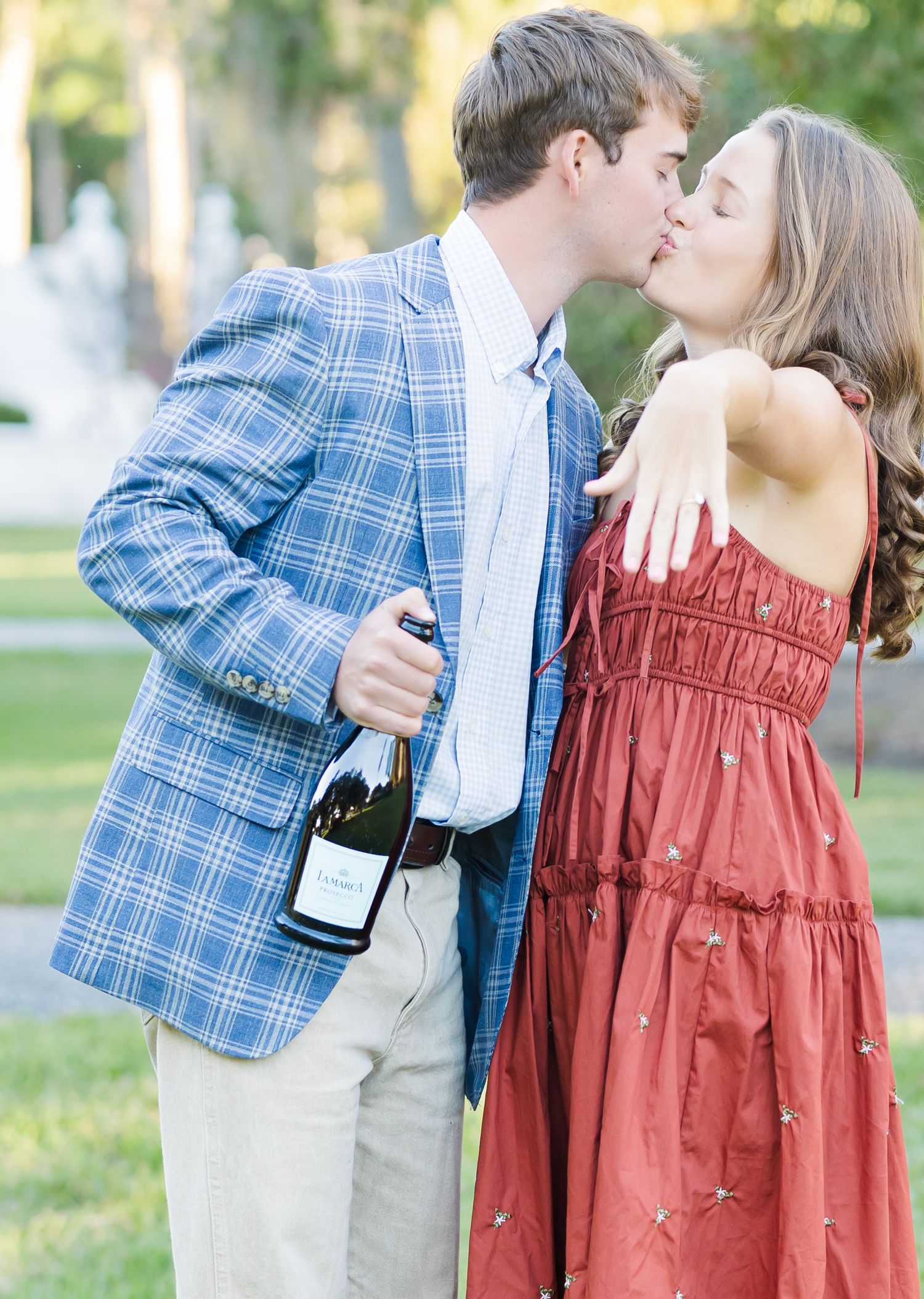 A romantic outdoor photoshoot shows a couple in a blue plaid blazer and rust-colored dress sharing tender moments.