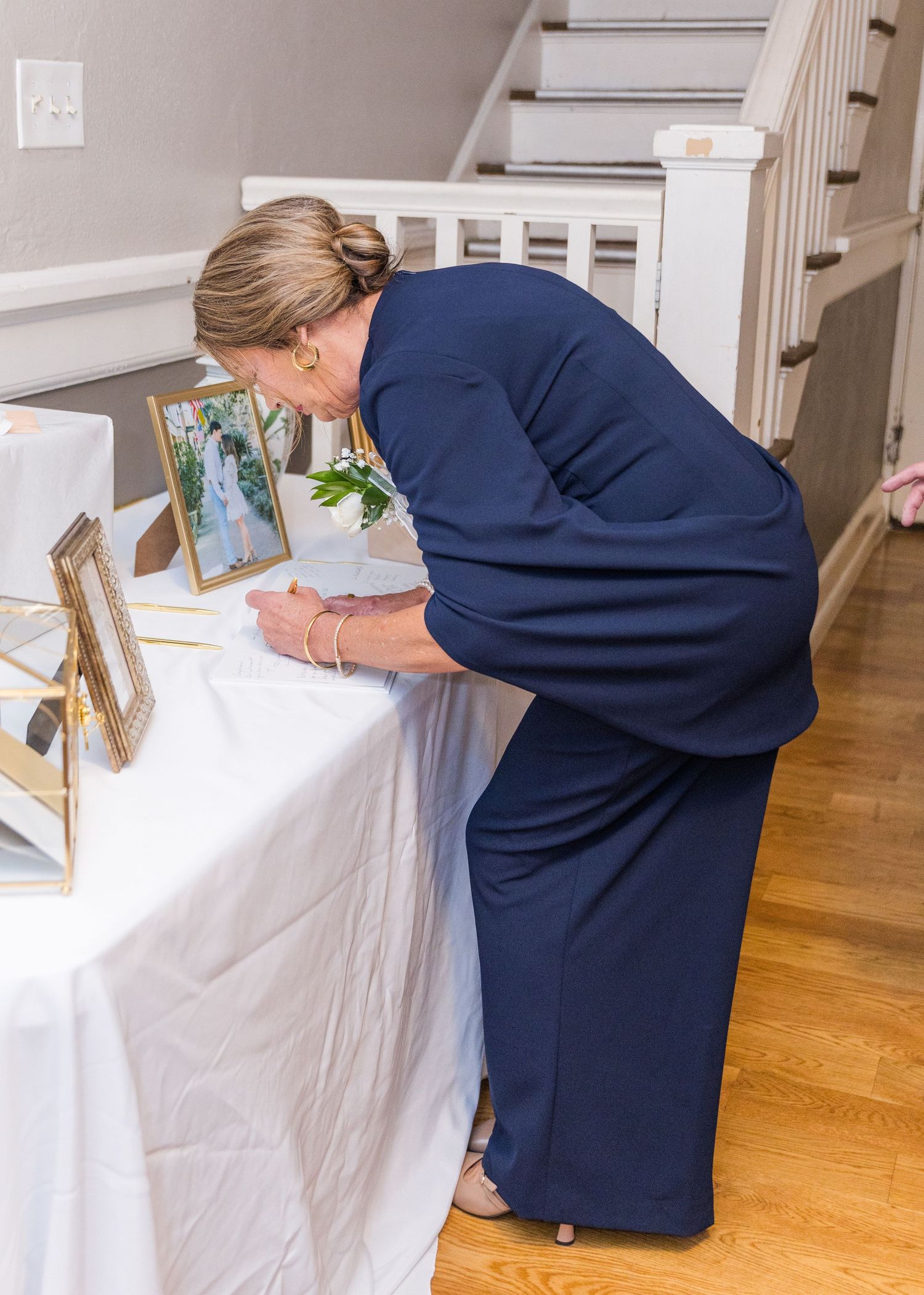 Woman in navy dress signing guest book at elegant wedding reception table with framed photos.