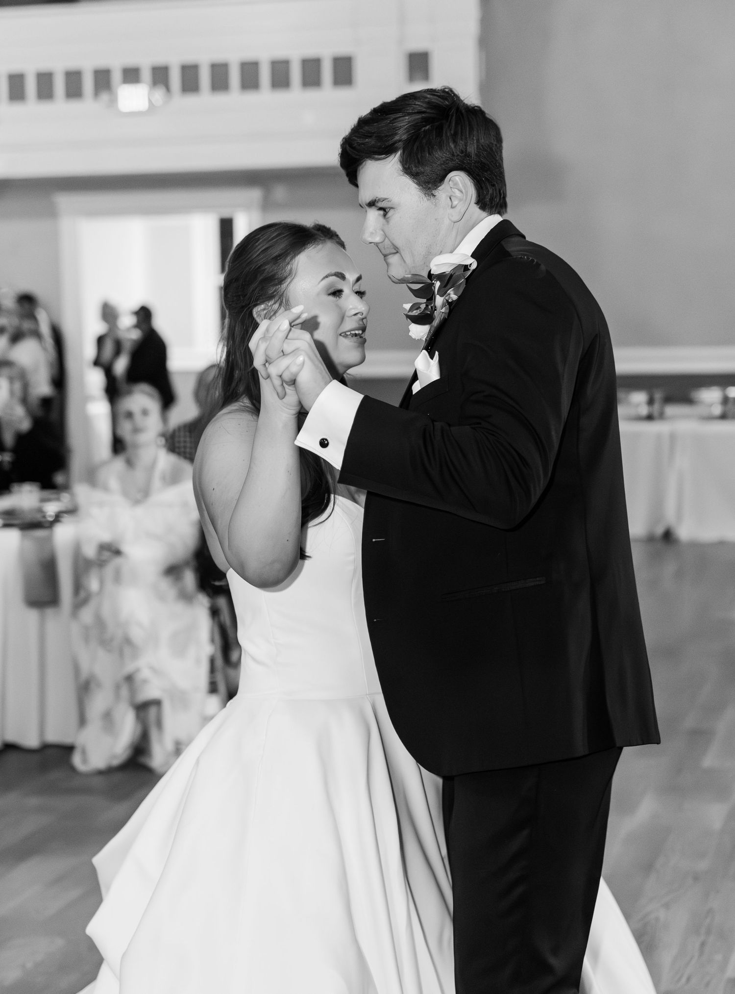 Black and white photo of groom wiping bride's tears during emotional first dance at wedding reception.