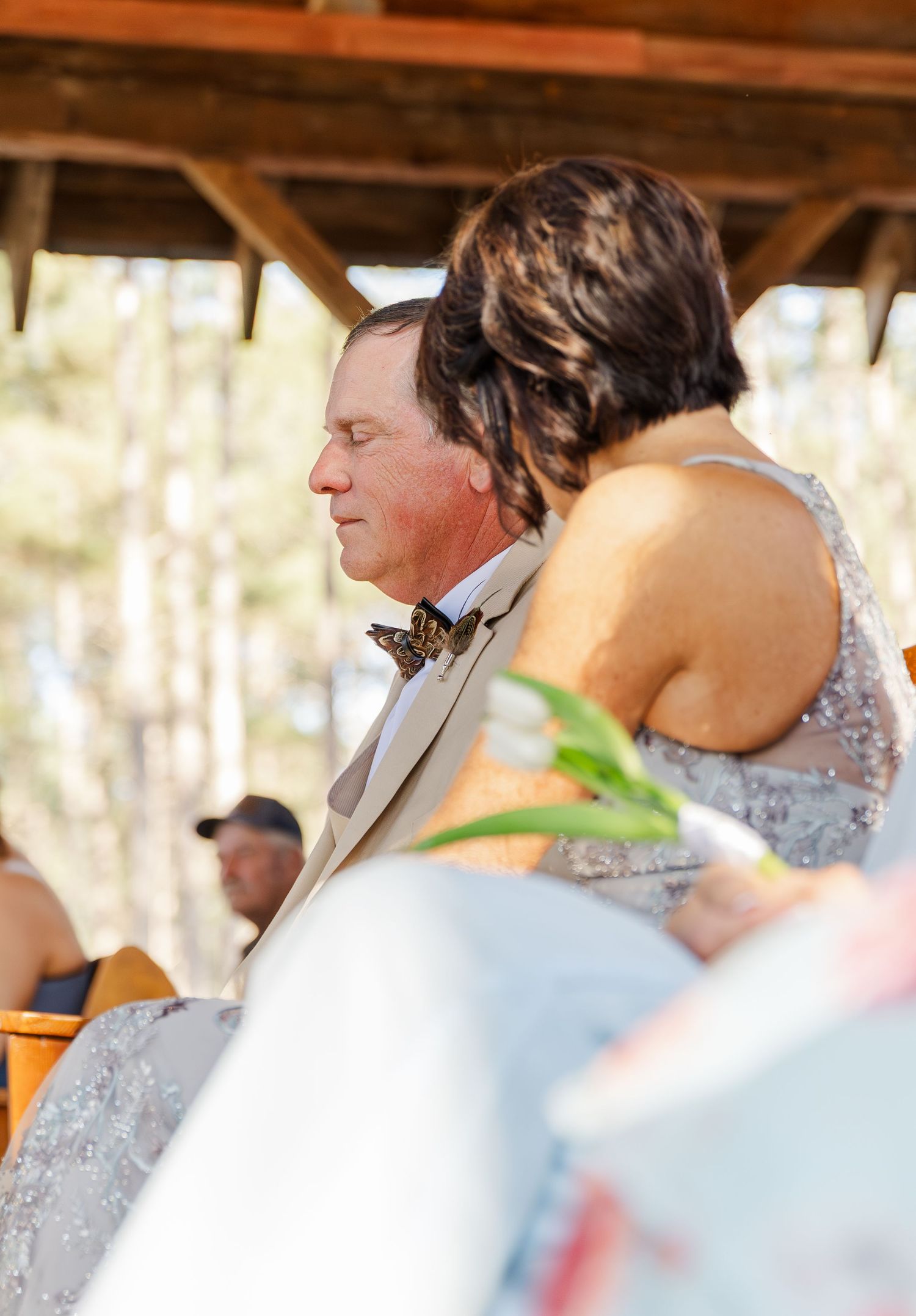 Father of the bride in cream suit with butterfly bow tie shares tender moment during wedding ceremony.