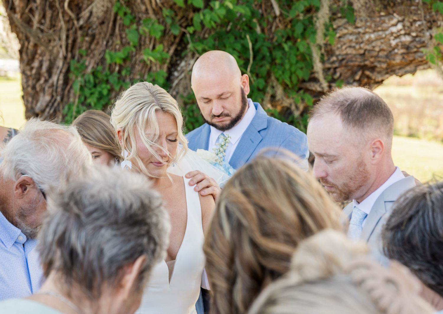 Bride and groom exchange rings during an intimate outdoor wedding ceremony surrounded by guests.