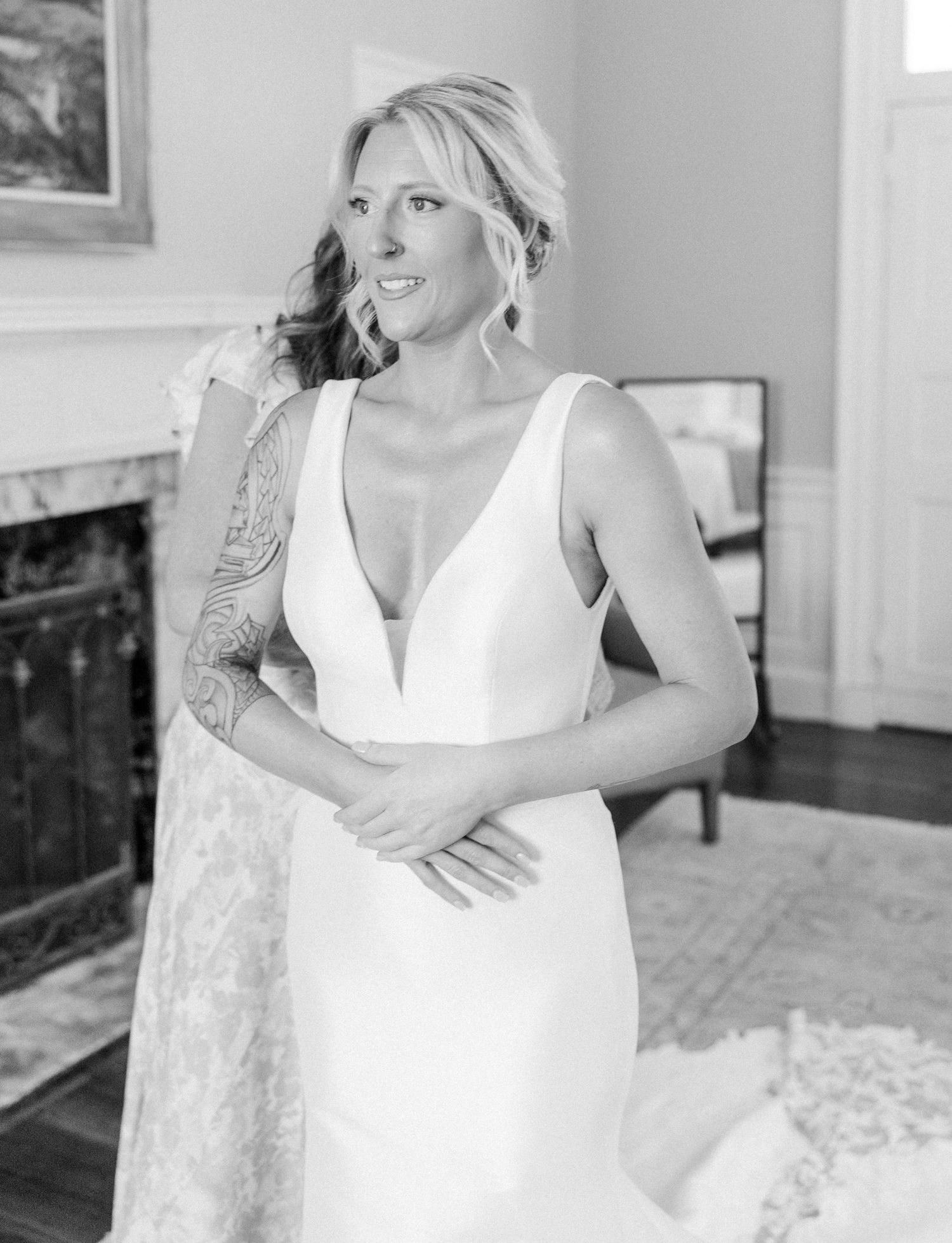Black and white portrait of blonde bride in deep V-neck wedding gown with floral arm tattoo.