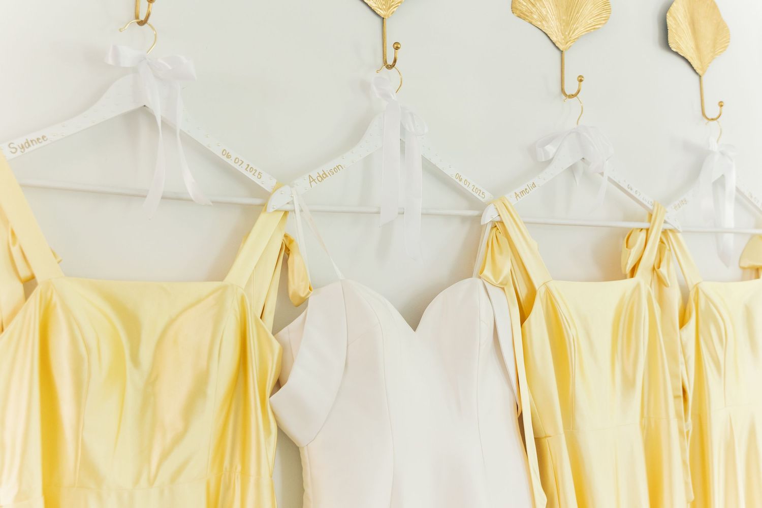 Yellow and white bridesmaid dresses hanging neatly on white hangers against a light background.