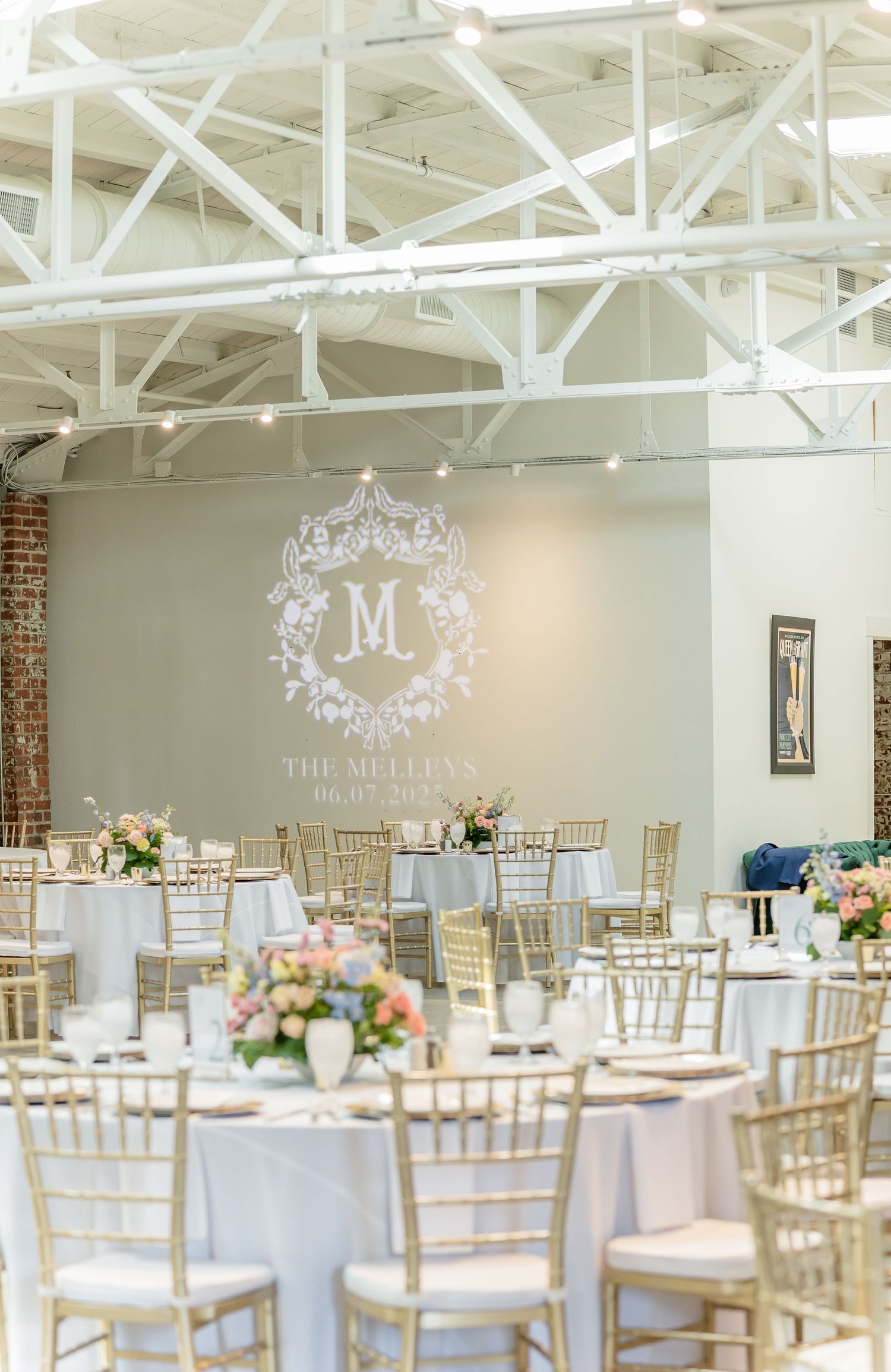 Elegant white and gold wedding reception venue with monogrammed wall decorations and chiavari chairs.