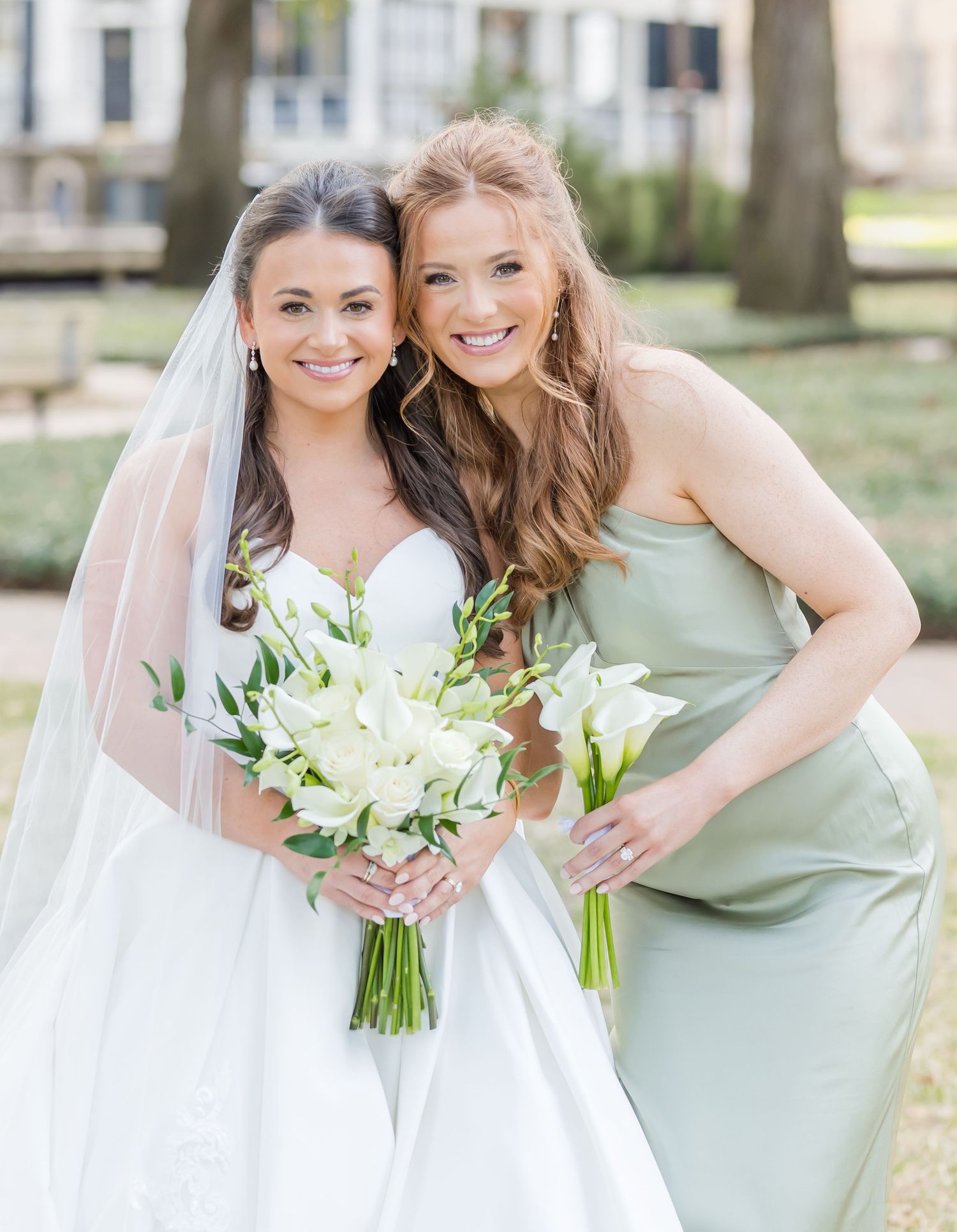 Bride and bridesmaid share joyful moment in mint green and white dresses with floral bouquets.