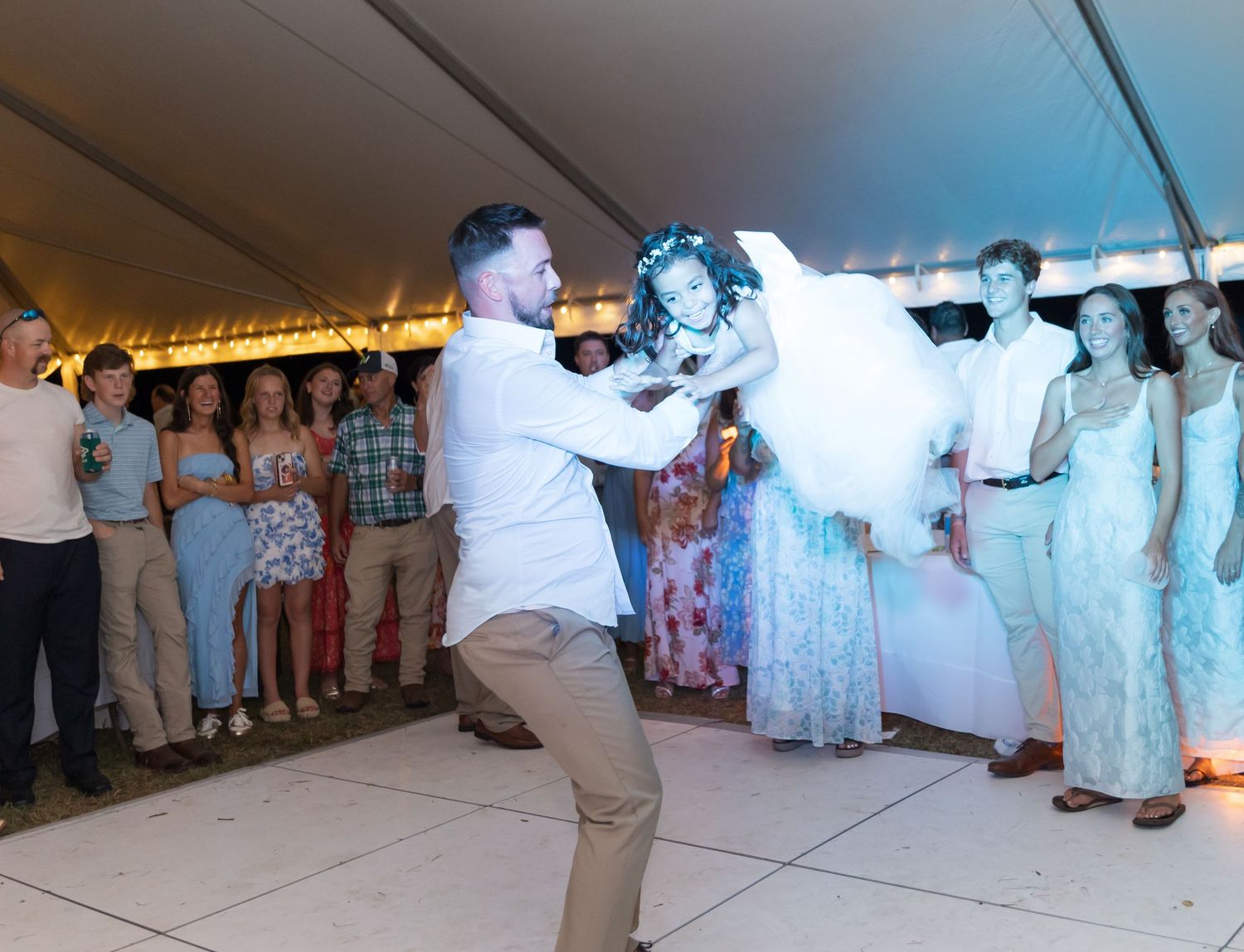 People dancing in a line at an outdoor event wearing traditional white and floral dresses.