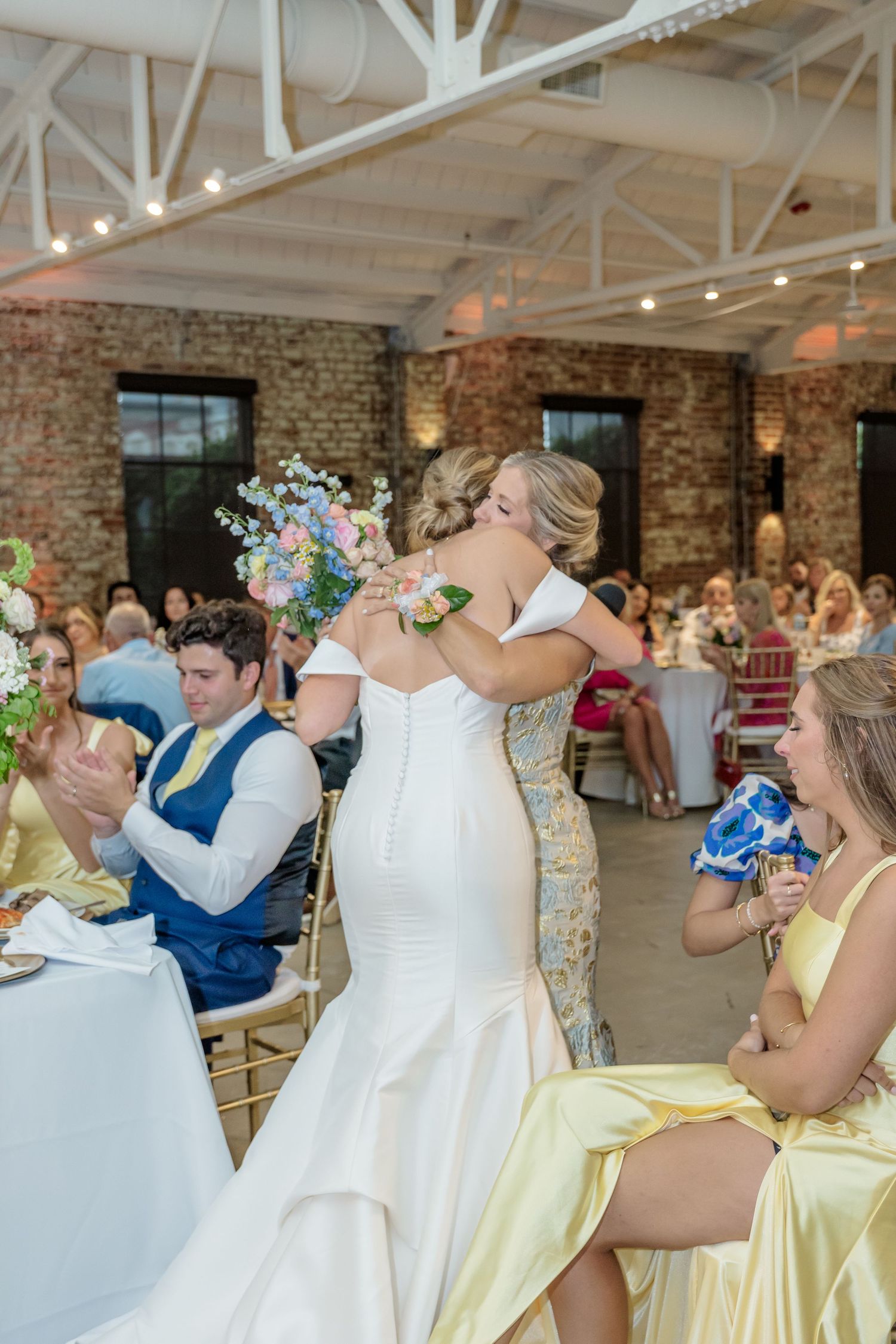 Bridesmaids in yellow and white dresses laughing together at a wedding reception.