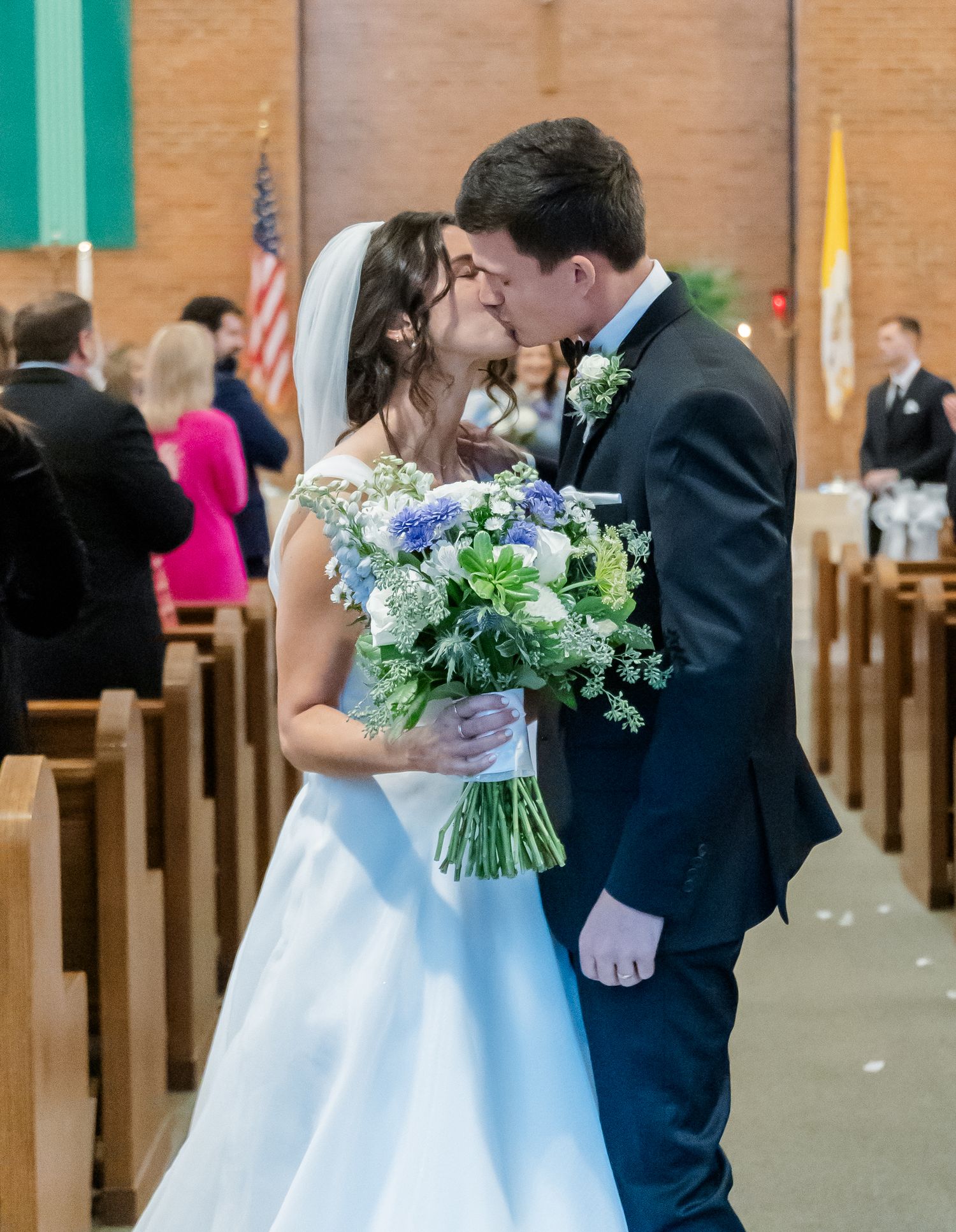 A wedding ceremony sequence showing a couple sharing their first kiss at the altar with a blue and white floral bouquet.