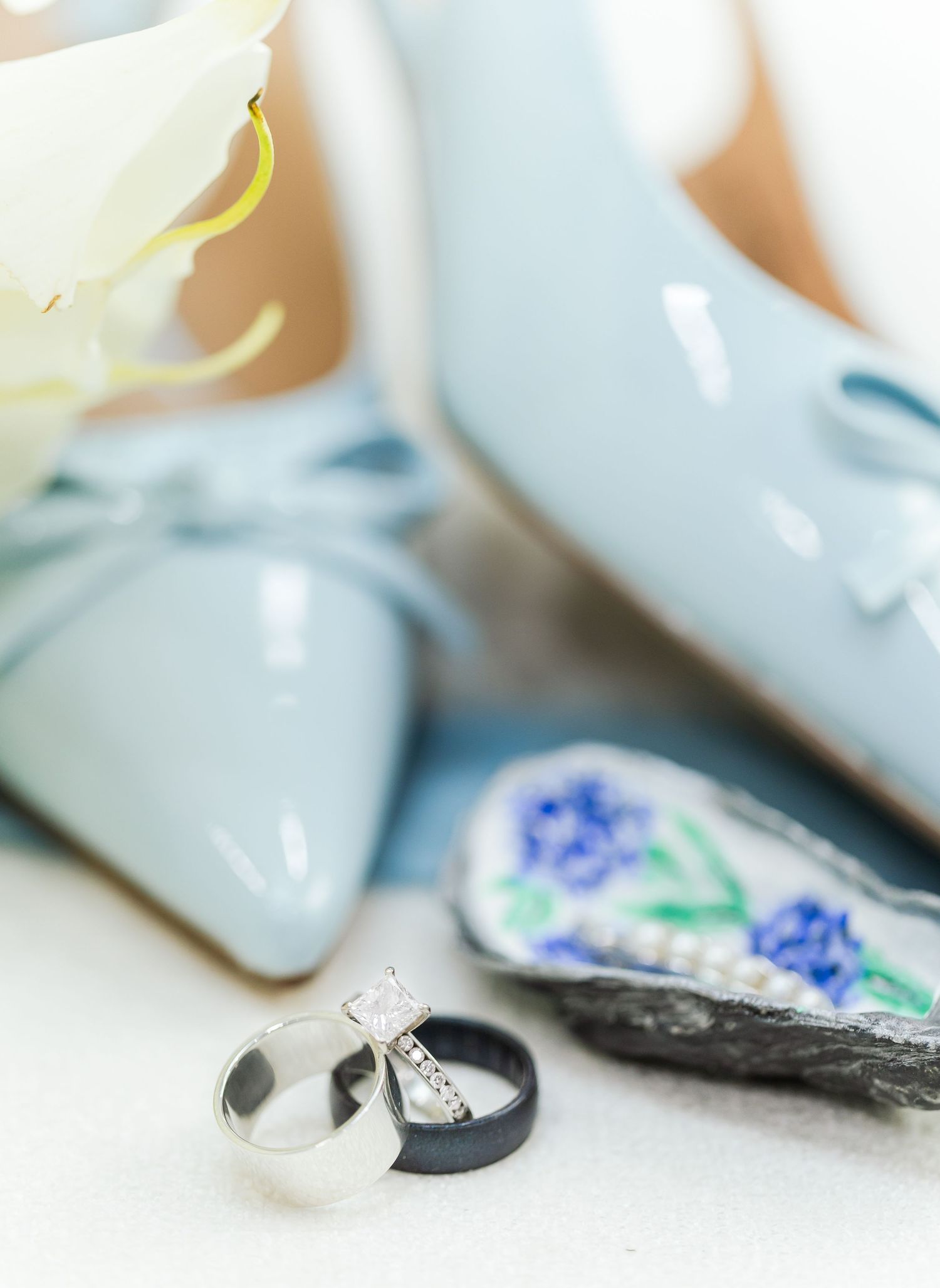 Wedding rings and engagement rings displayed on a soft white surface with blue and green floral elements in background.