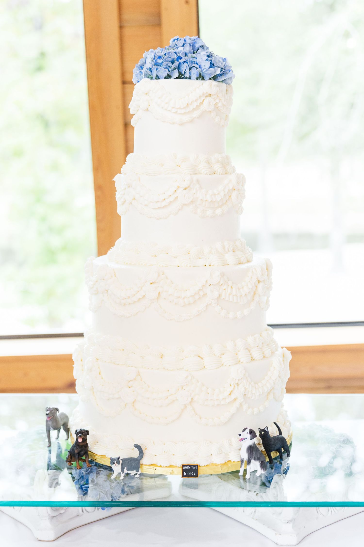 A white three-tiered wedding cake with delicate lace patterns and floral designs sits on a turquoise glass display stand.