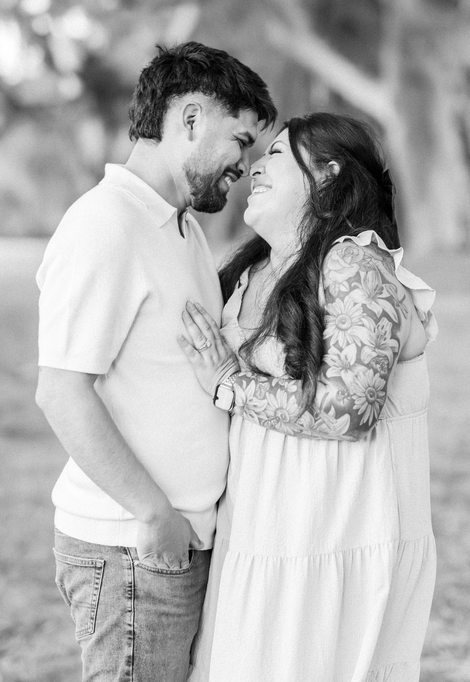 A couple shares an intimate moment in black and white under a canopy of trees.
