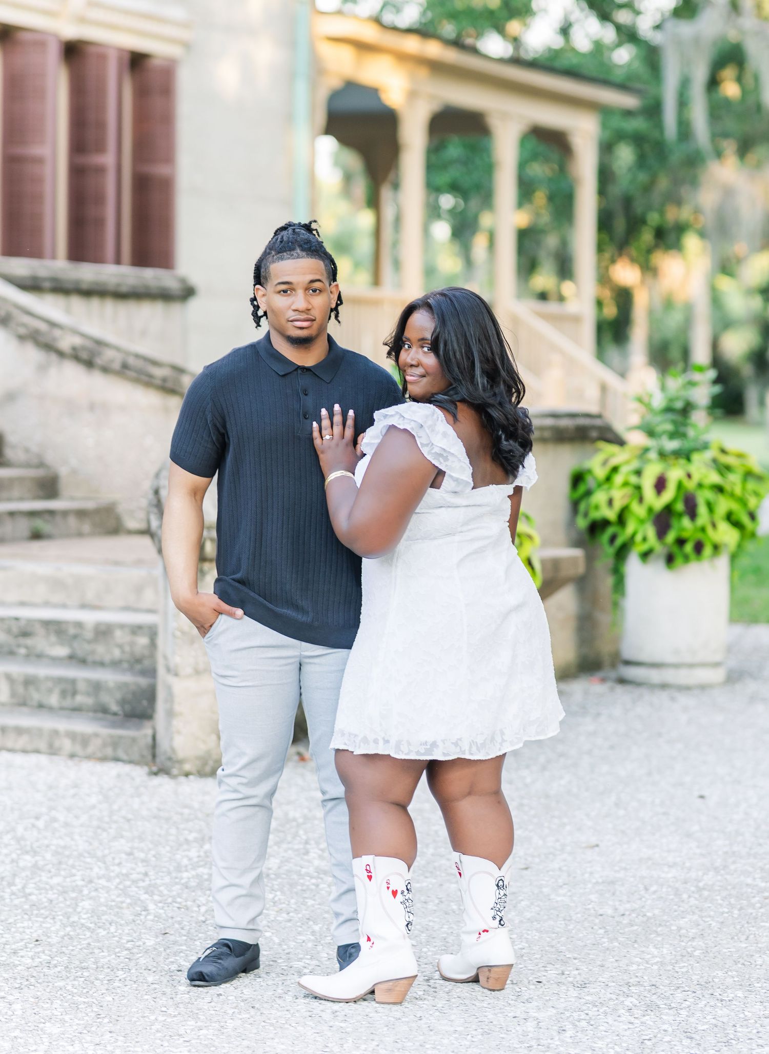 A couple poses together on stone steps with one person showing off a ring.