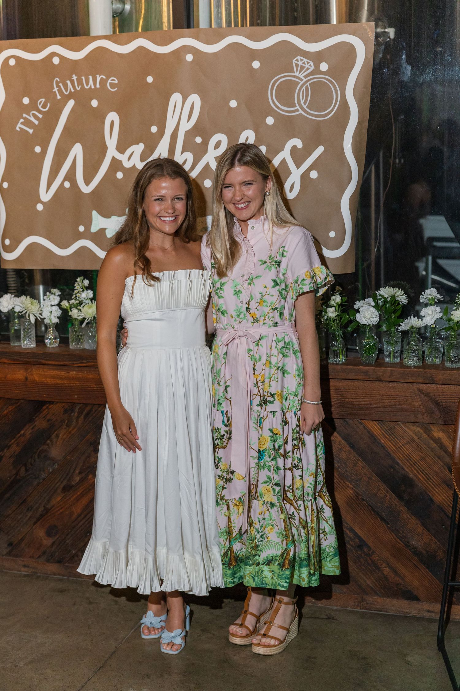 Two women posing together at a bridal shower in front of a The Future Walkers sign.