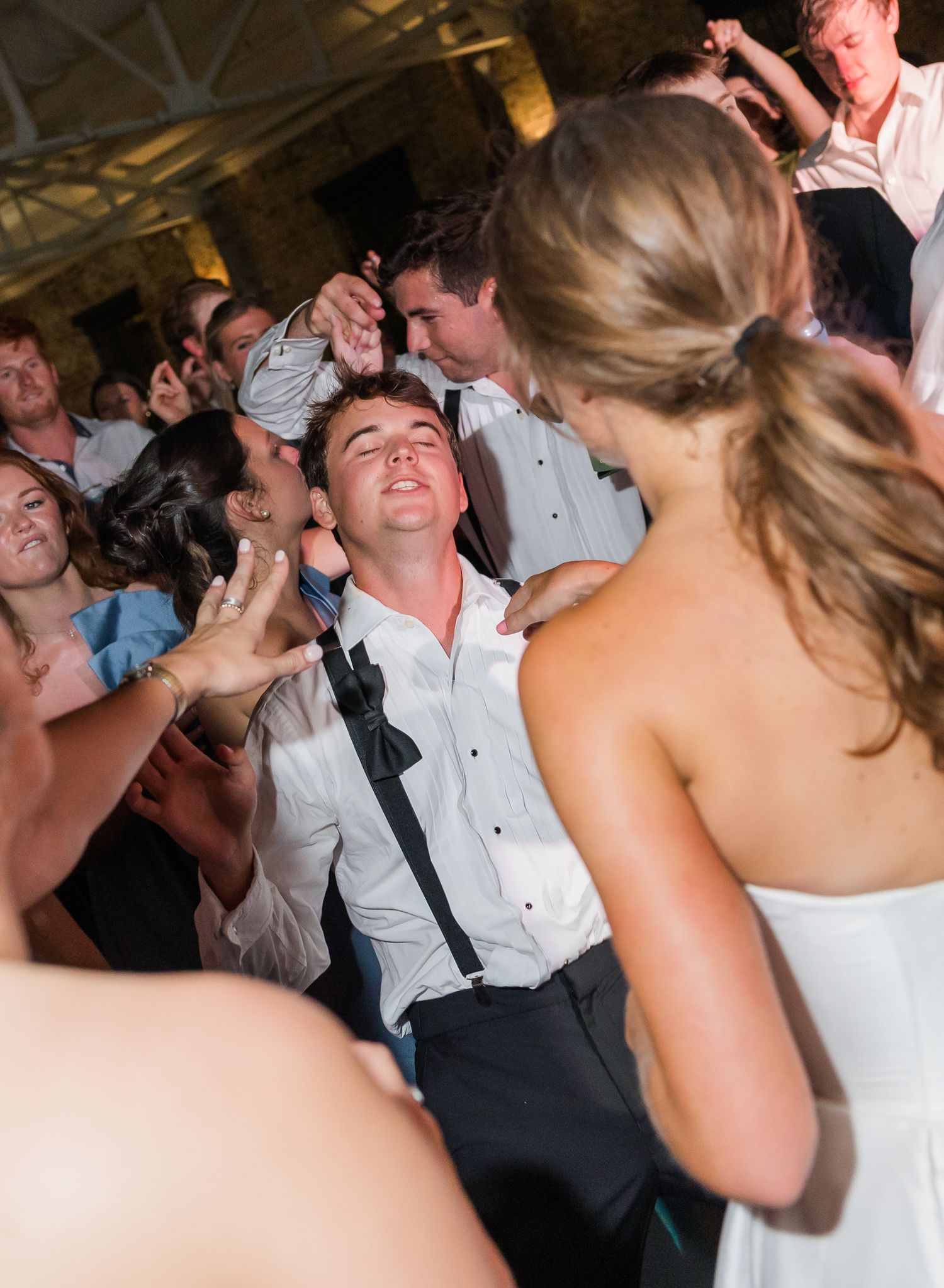 Energetic wedding guest dances enthusiastically on crowded reception dance floor in white dress shirt.