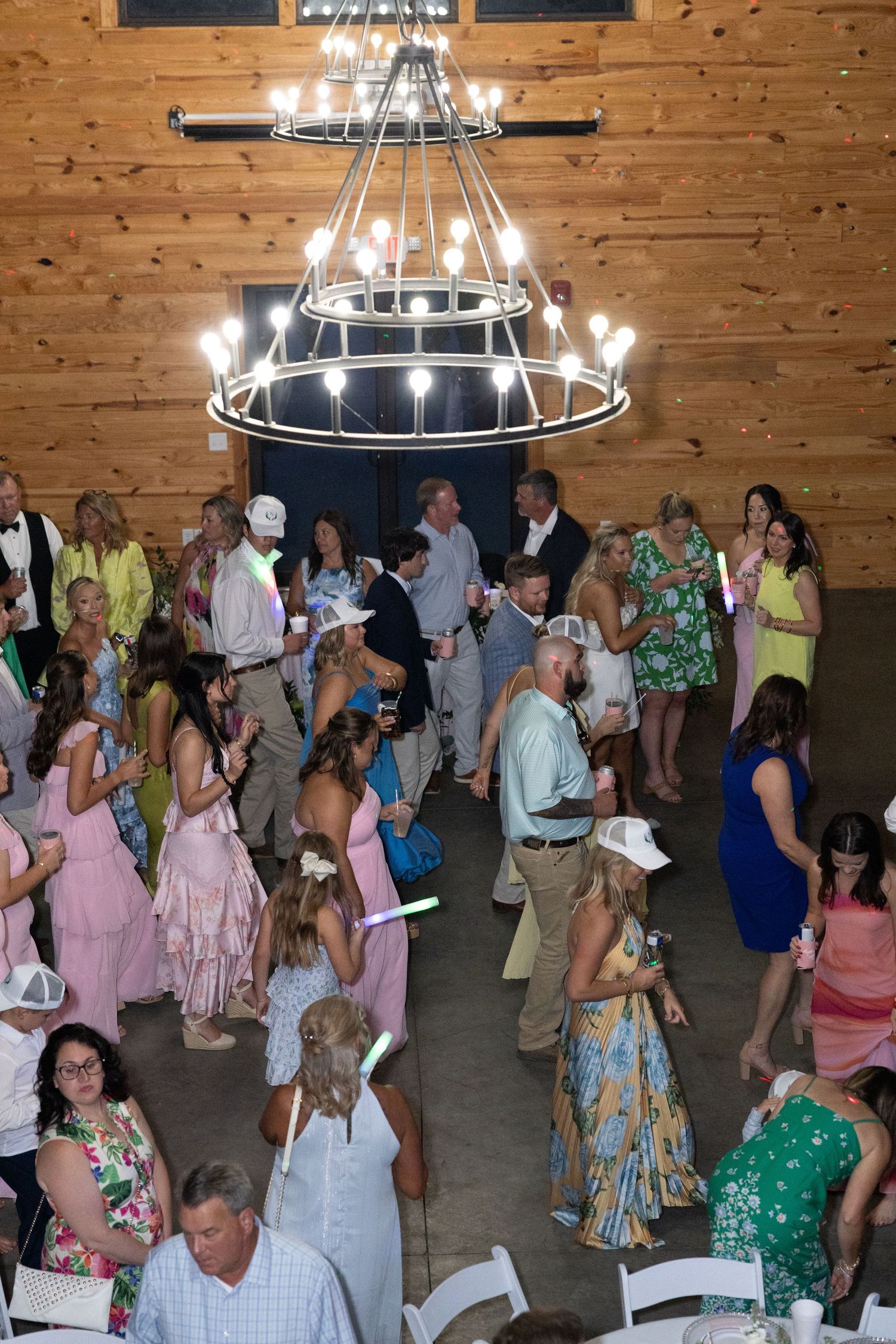Aerial view of wedding guests dancing under a chandelier in a rustic wood-paneled barn reception venue.