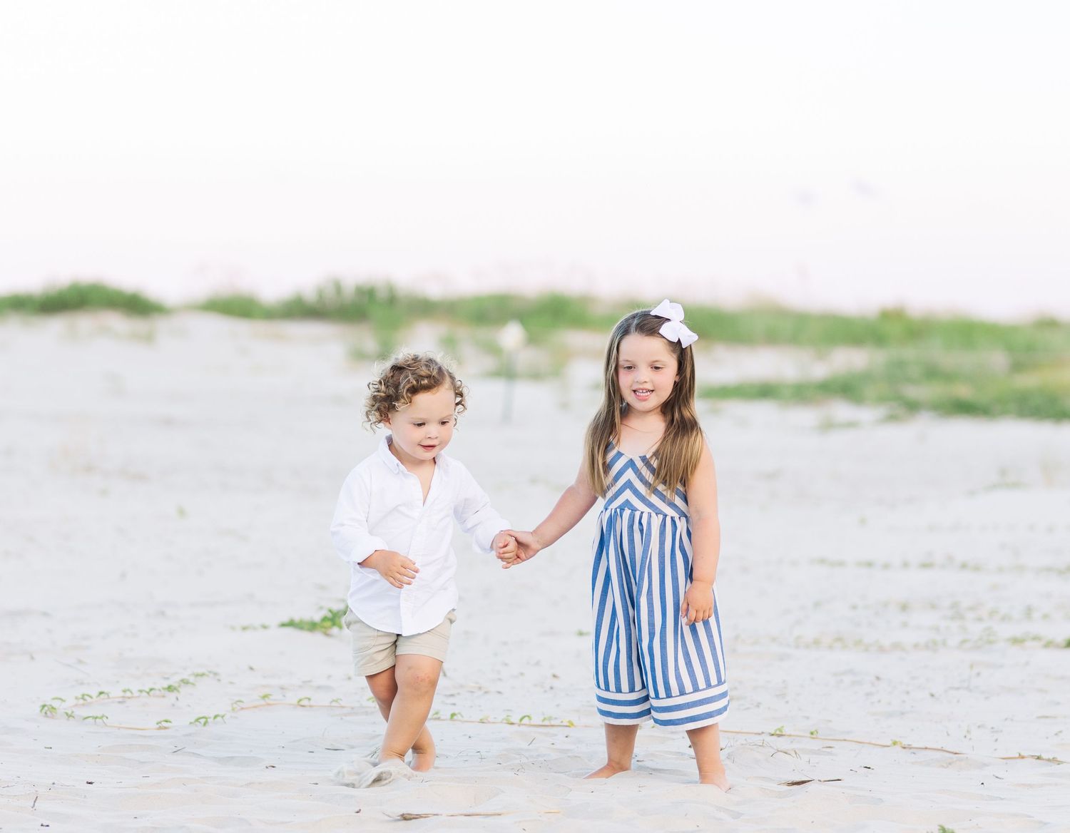Children playing together on a sandy beach wearing coordinated blue and white outfits.