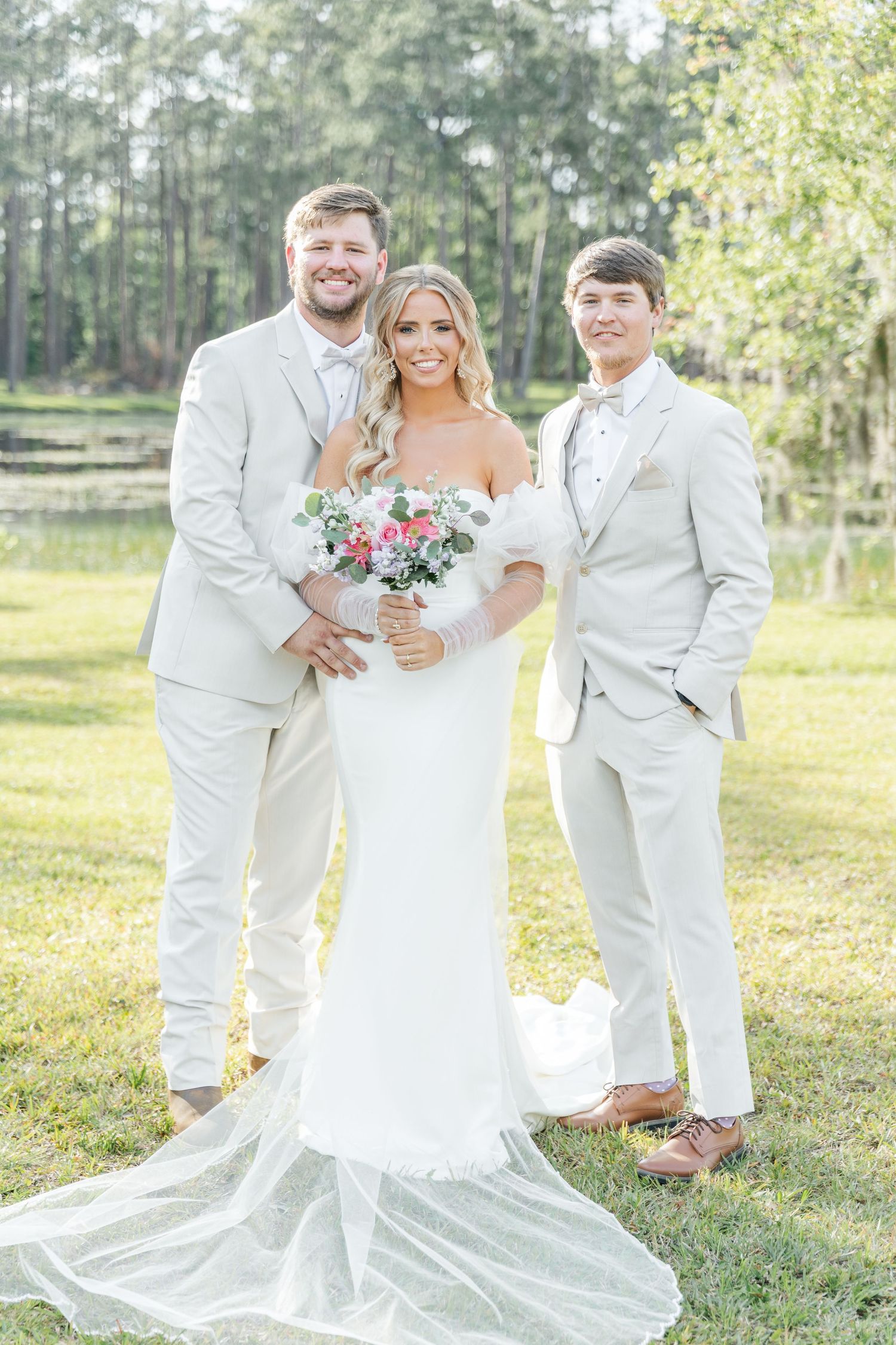 Outdoor wedding portrait of wedding party in crisp white attire with floral bouquet and long flowing veil.