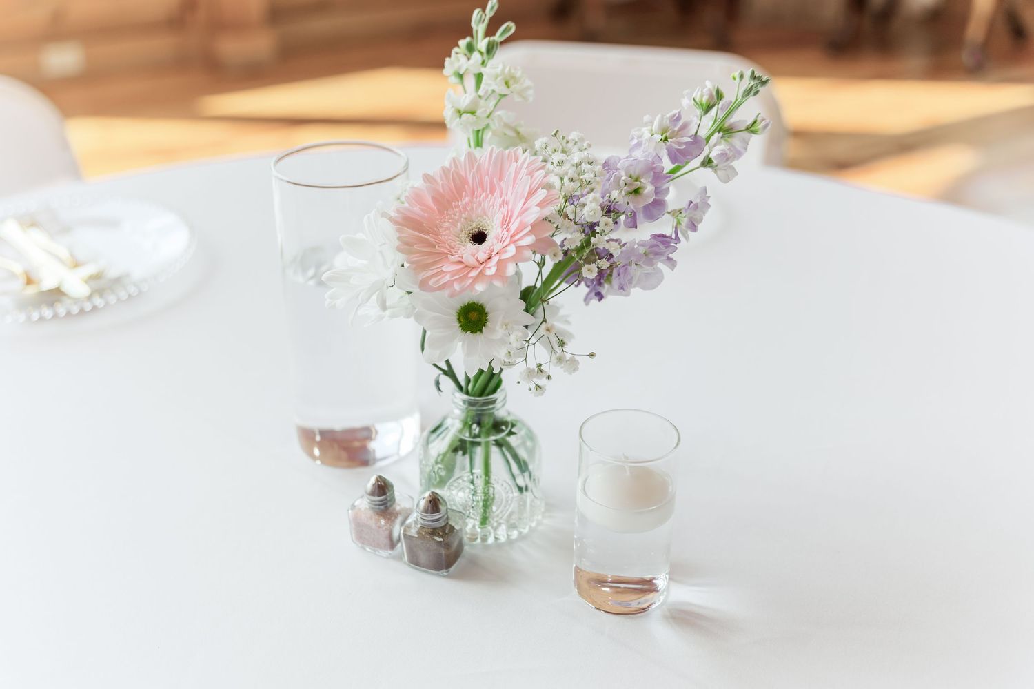 Fresh floral arrangement with pink gerbera daisy and purple flowers in mason jar on white table.