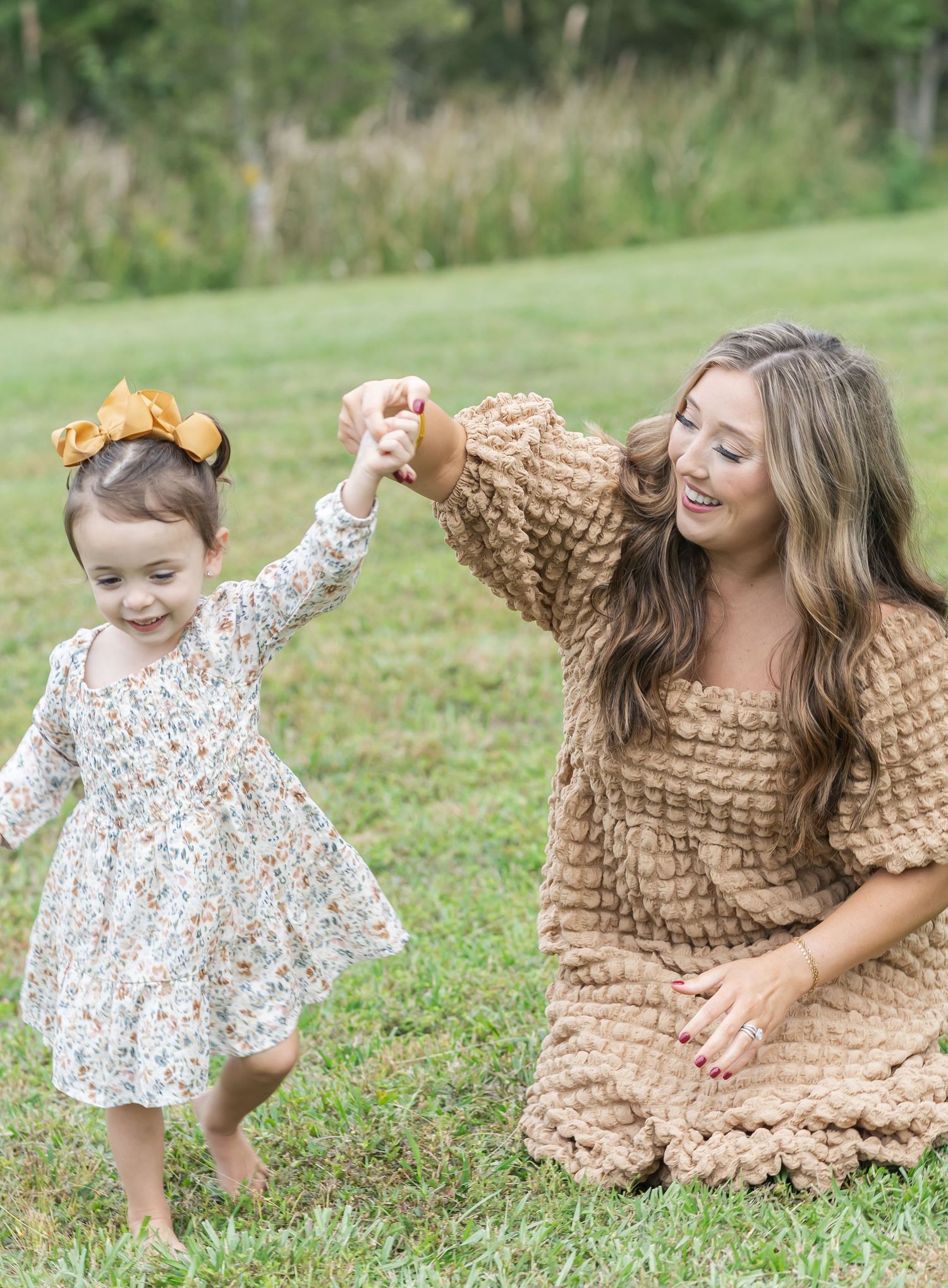 A joyful outdoor moment in a grassy field with matching floral and tan textured dresses.