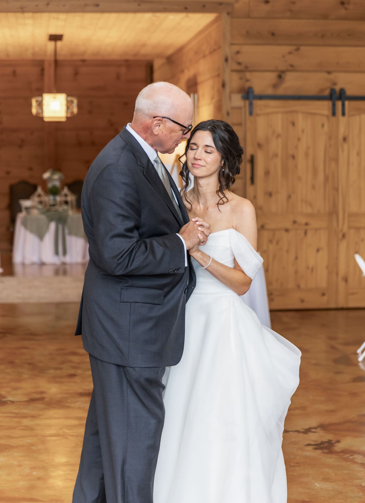 A tender dance moment in a rustic wooden venue during a wedding reception.