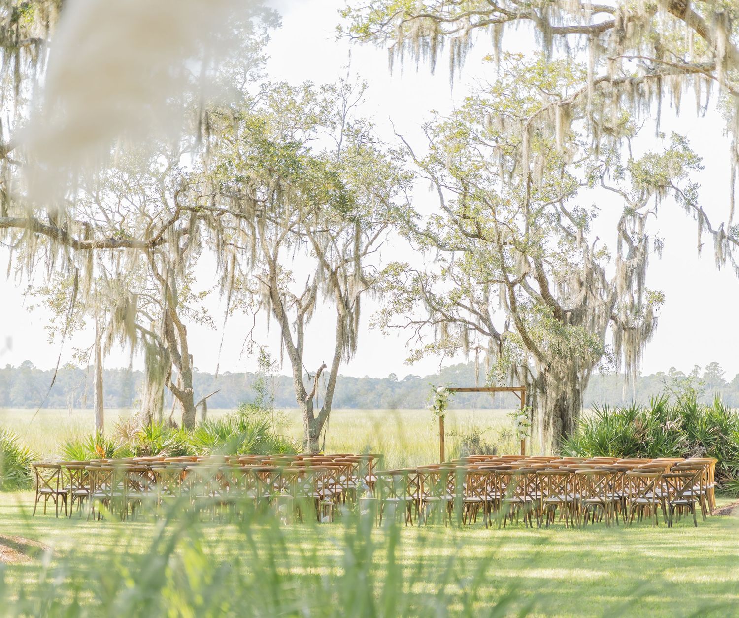Rustic wooden chairs arranged in rows under Spanish moss draped oak trees for an outdoor wedding ceremony.