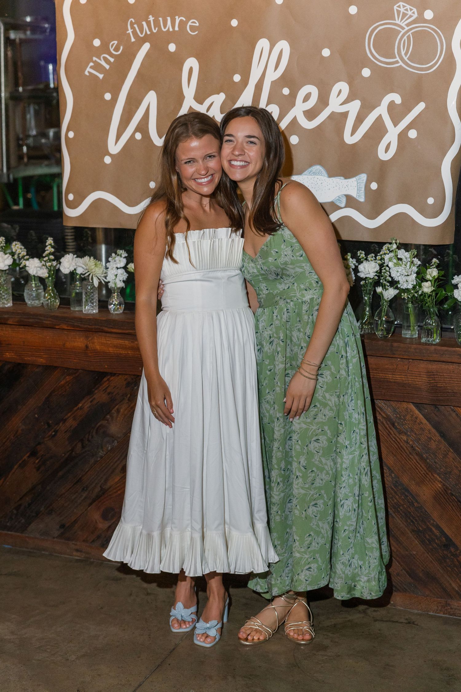 Two women smile together at engagement party before 'The Future Walkers' decorative banner.