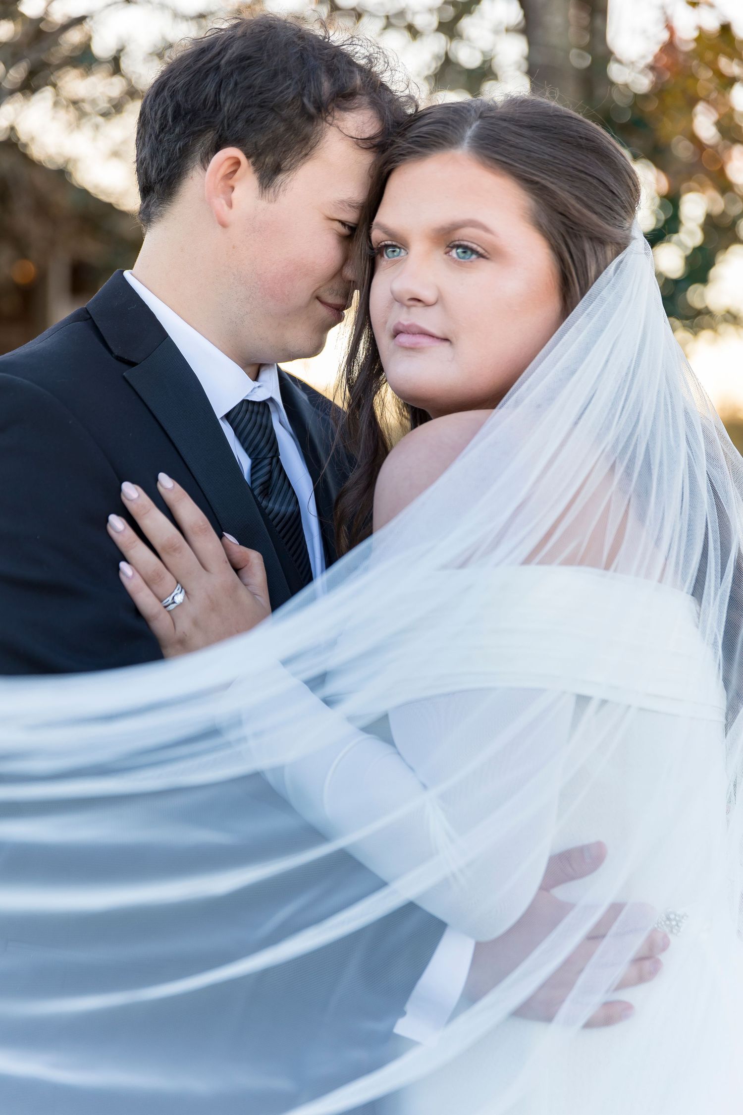 Romantic outdoor wedding portrait with flowing veil and intimate pose.