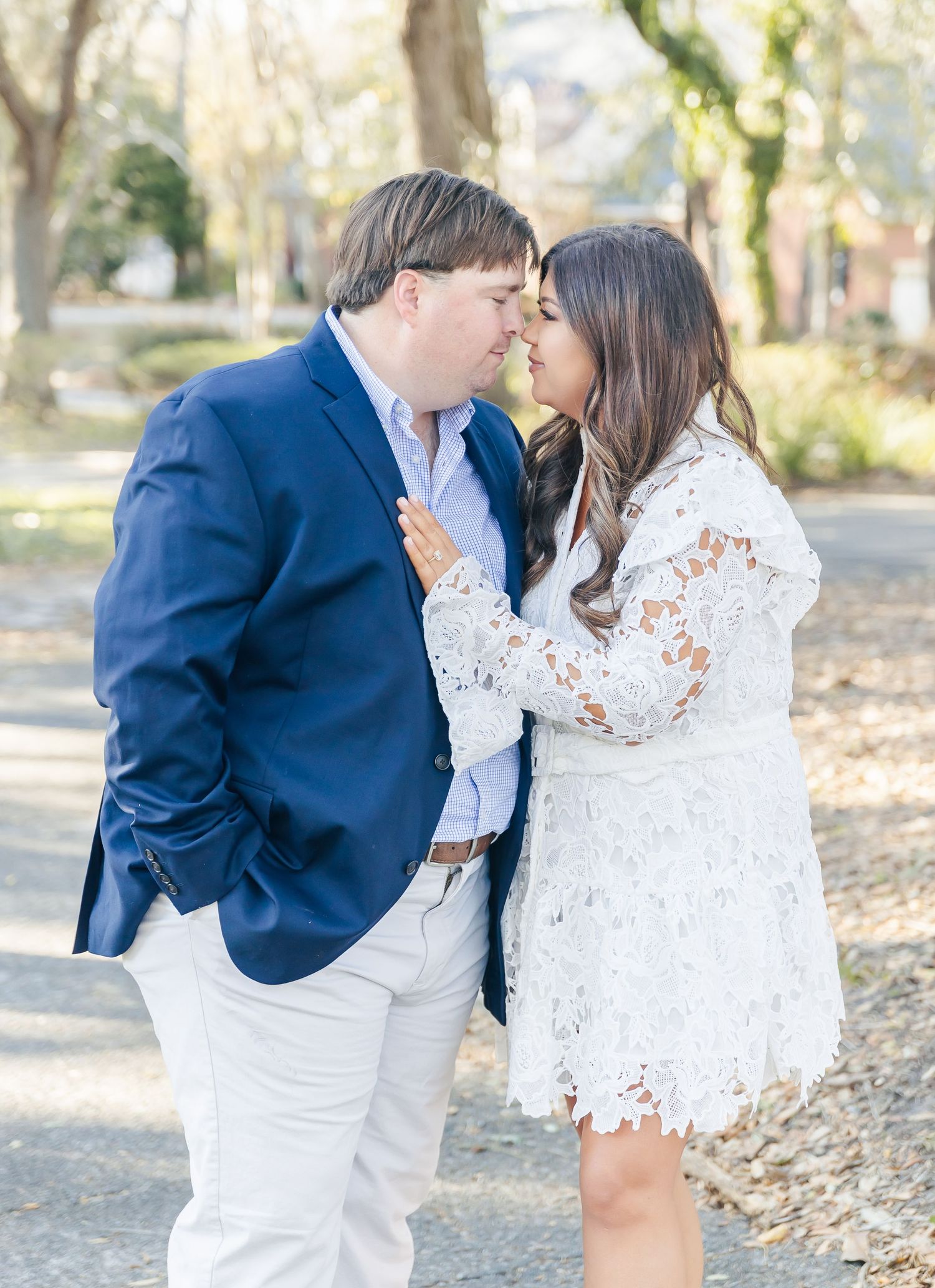 A romantic couple shares an intimate moment while dressed in formal attire on a wooded path.