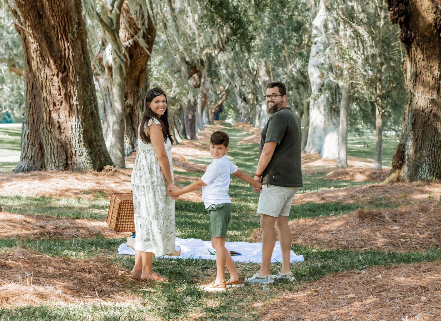 Family strolling along a tree-lined path carrying a picnic basket on a sunny afternoon.