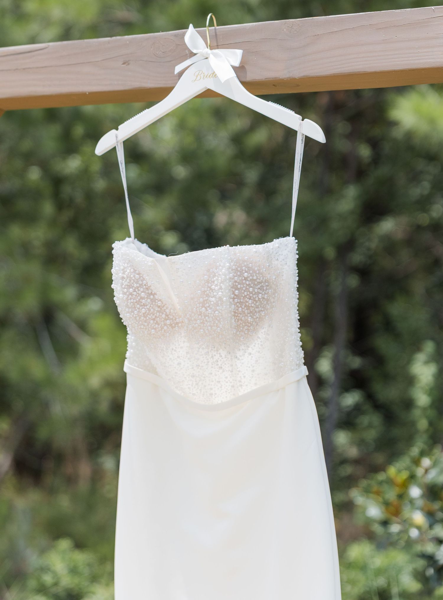 Elegant strapless white wedding dress with beaded bodice hanging on a white hanger outdoors.