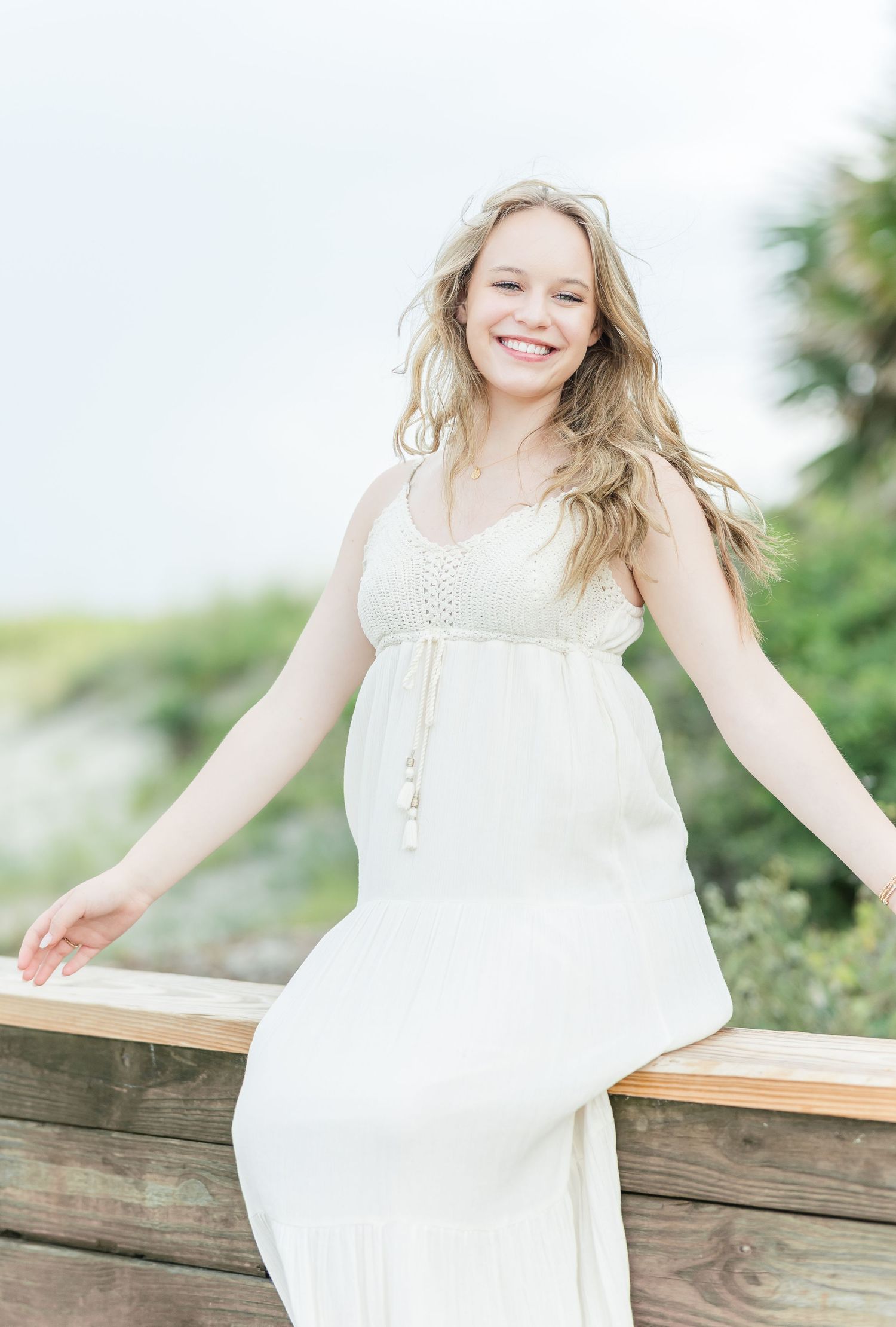Ethereal outdoor portrait in a white lace dress against natural greenery and wooden railing in soft lighting.