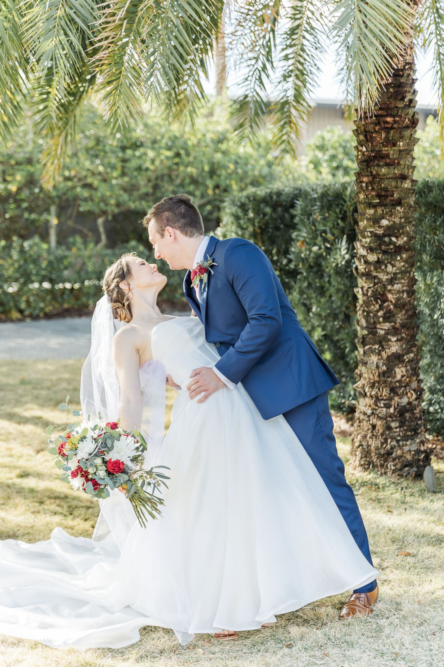 A romantic wedding portrait under palm trees with the couple sharing a kiss.
