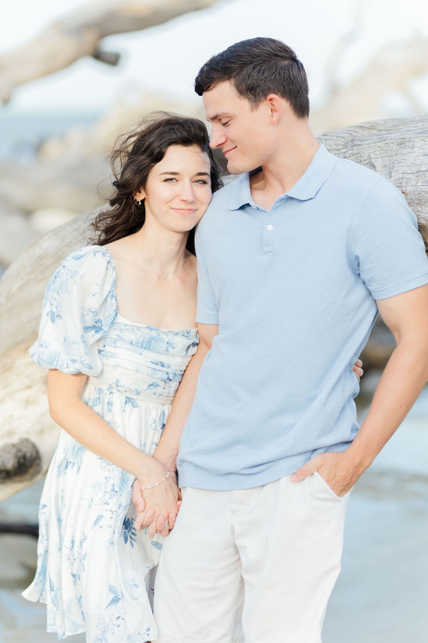 A couple in coordinating blue and white outfits poses against a coastal backdrop.