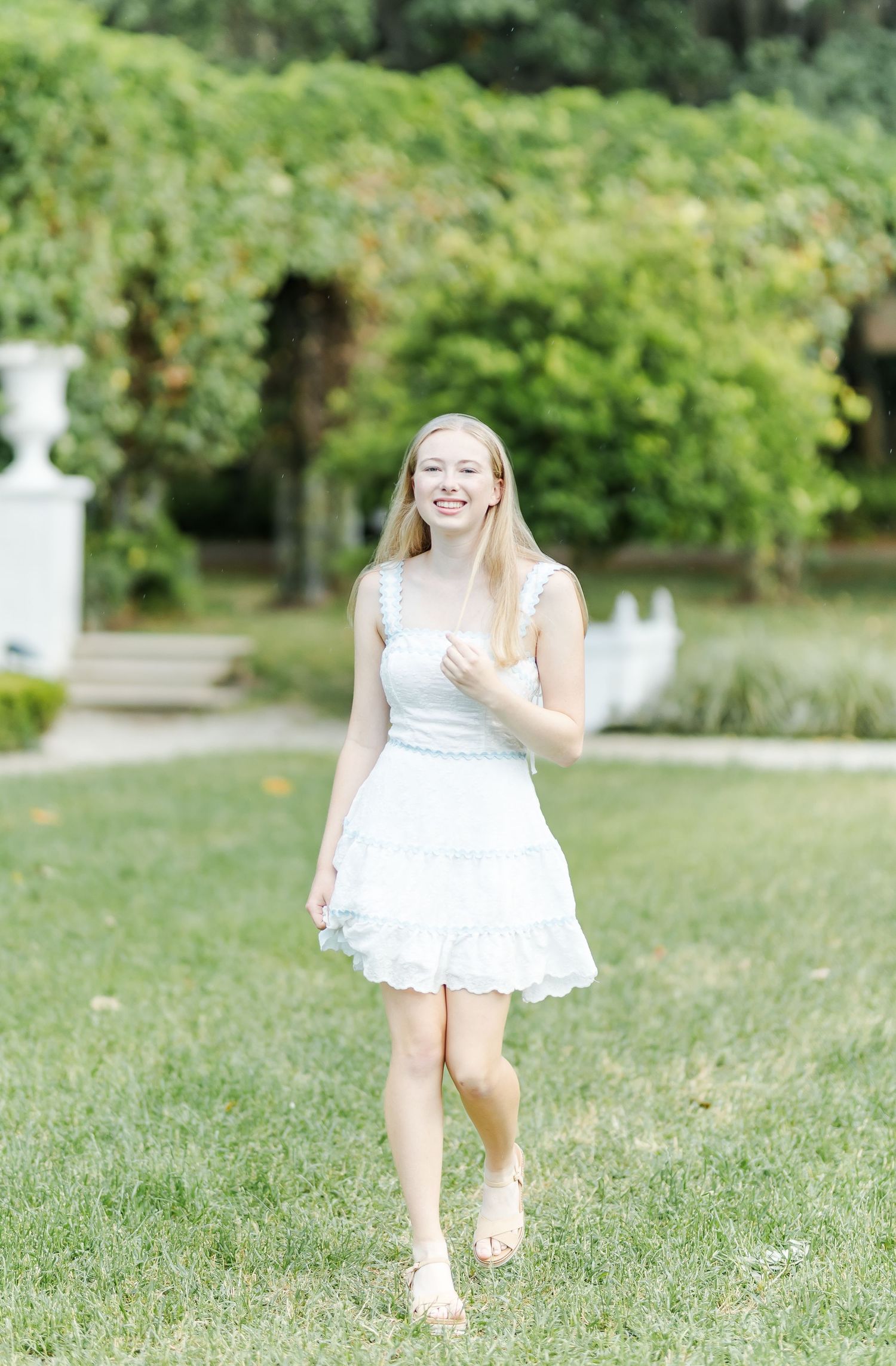 Someone in a white summer dress running and playing on green grass with trees in background.