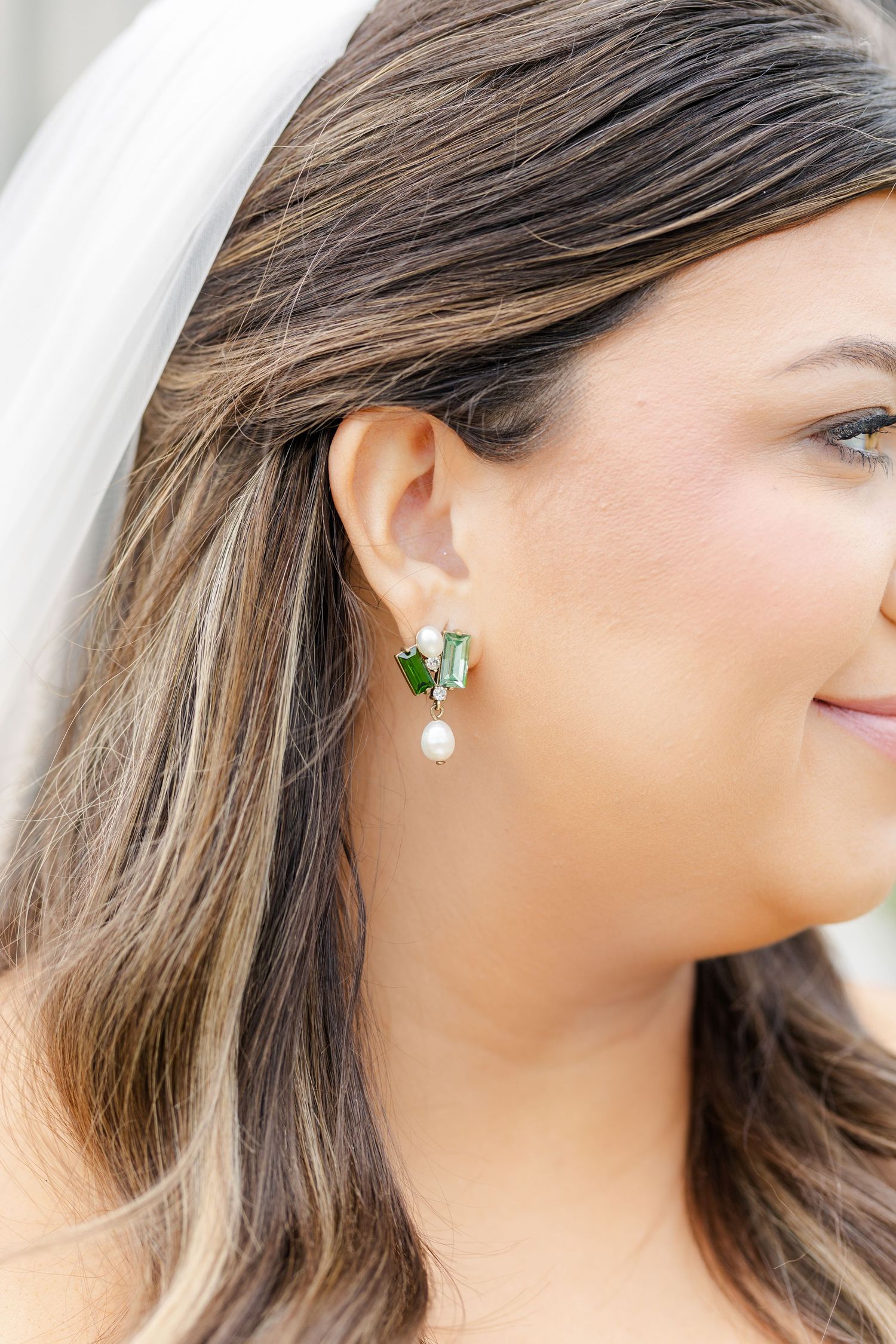Bride wearing elegant green crystal and pearl drop earrings with white wedding veil in her brunette hair.