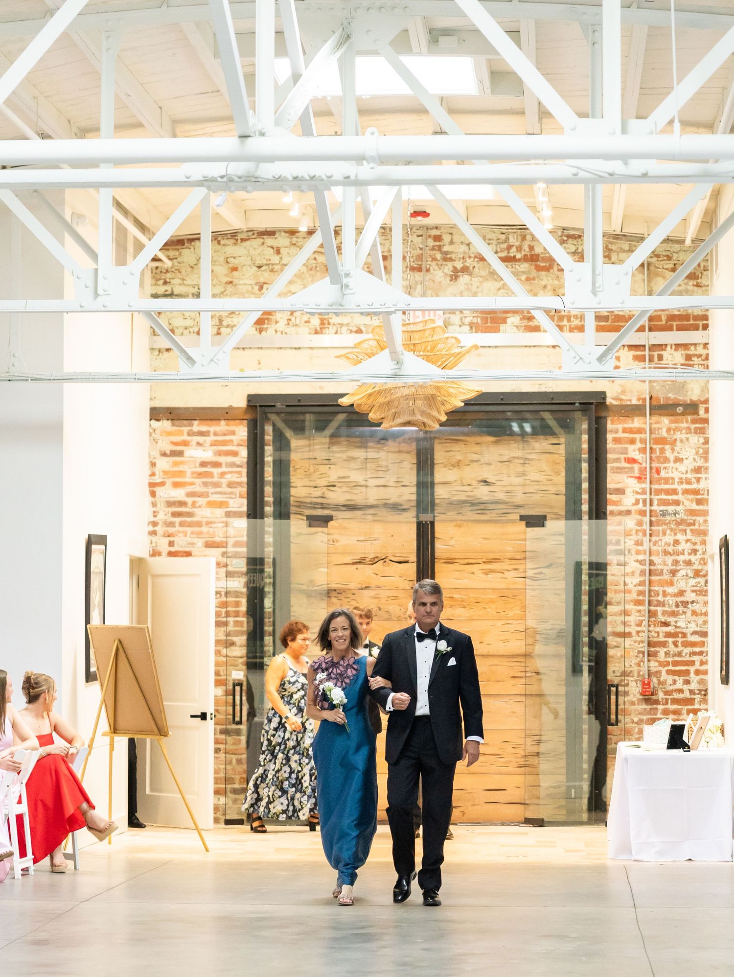 Couple makes grand entrance through elegant glass doors at industrial brick wedding reception venue.