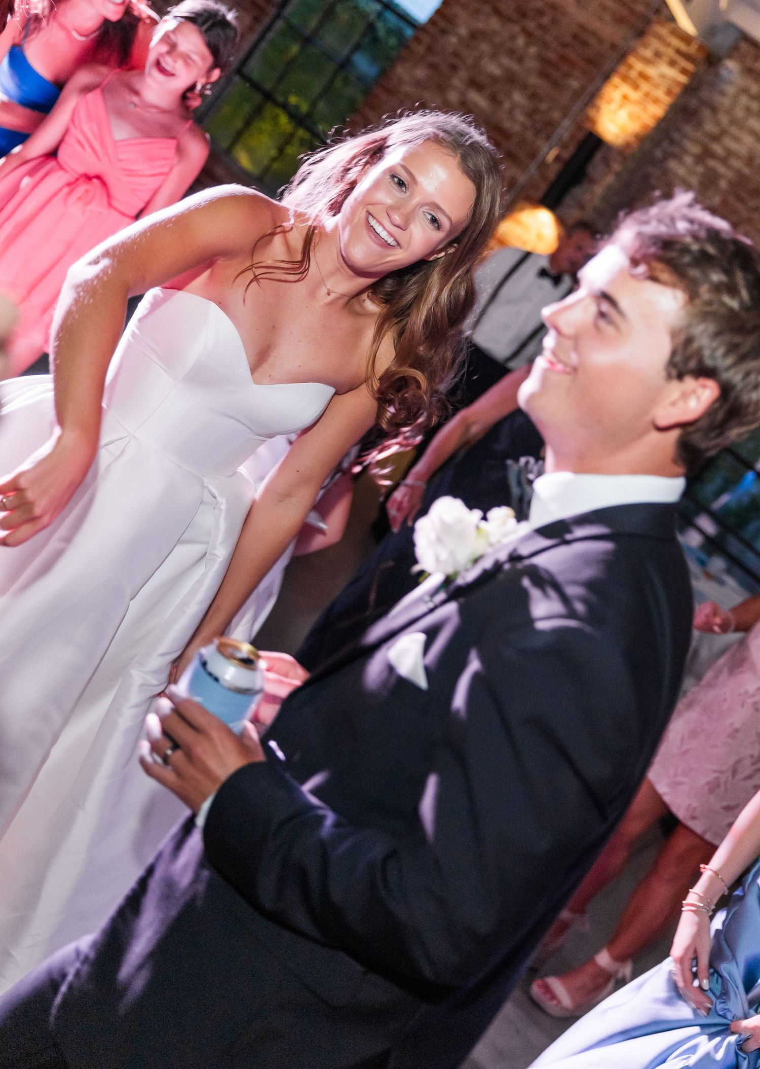 Bride in strapless white gown laughs with groom during lively outdoor wedding reception celebration.