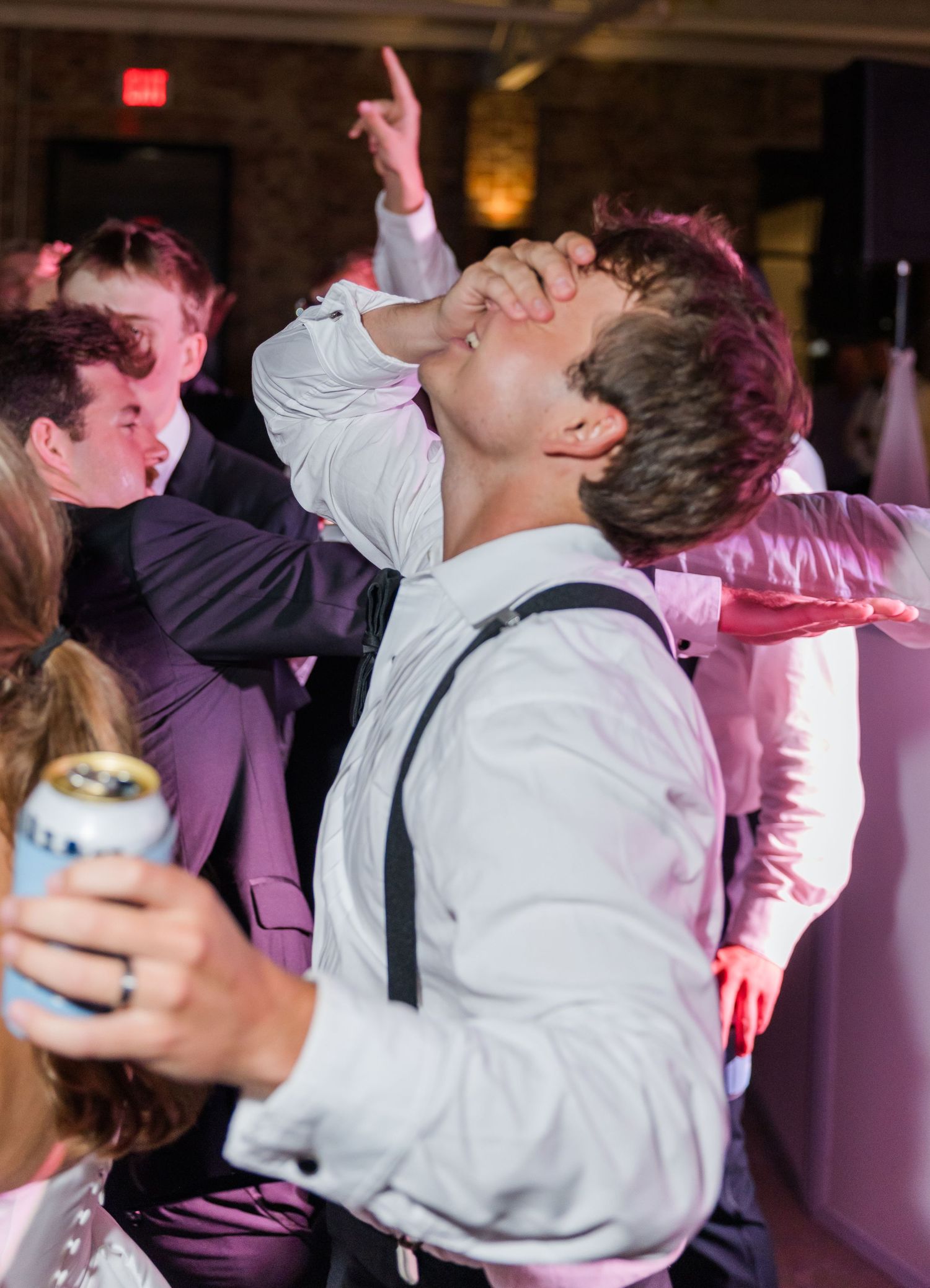 Energetic wedding guest in white shirt and suspenders dances enthusiastically on the reception dance floor.