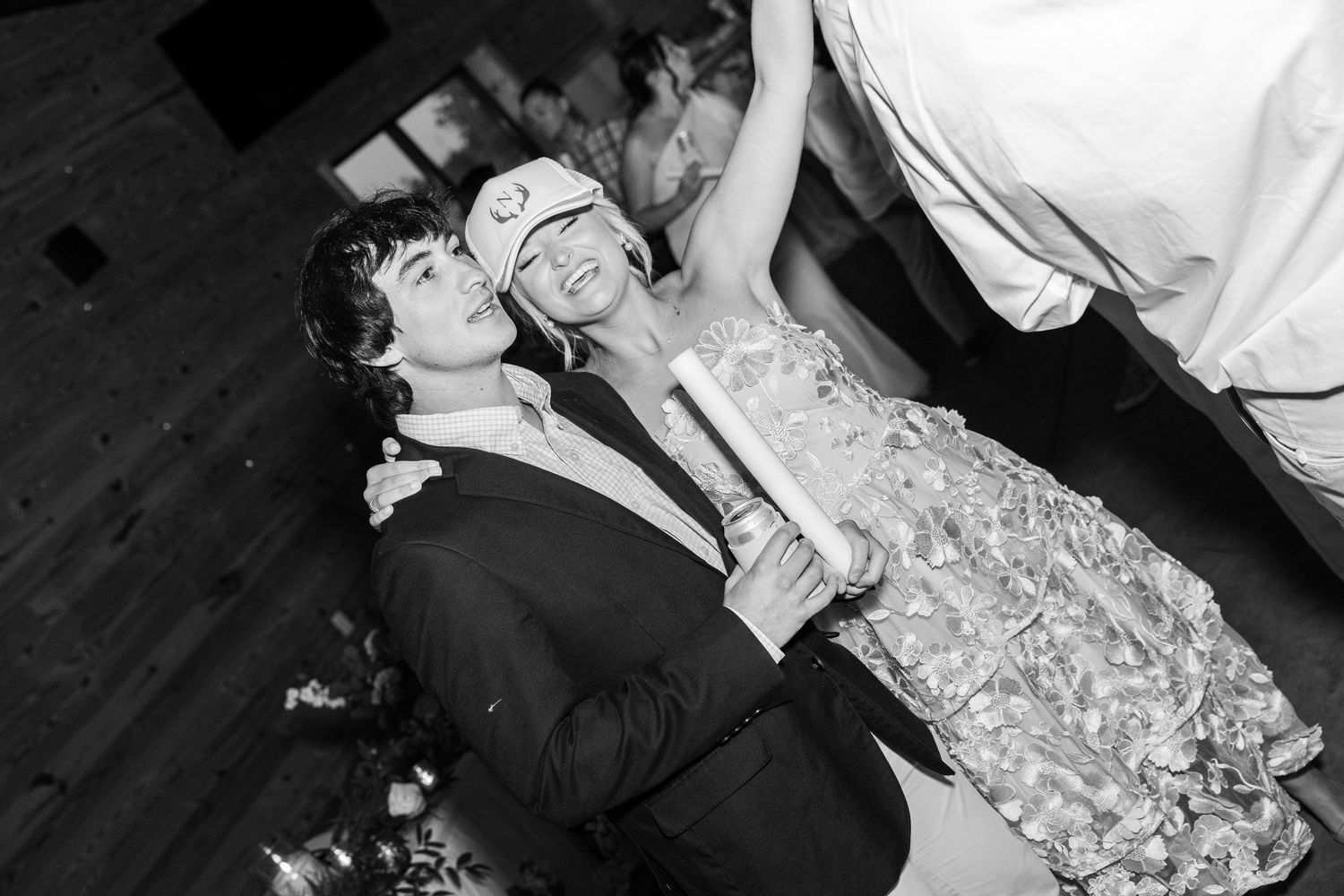 Couple celebrating at a wedding reception, groom in tuxedo and bride in floral dress dancing joyfully.