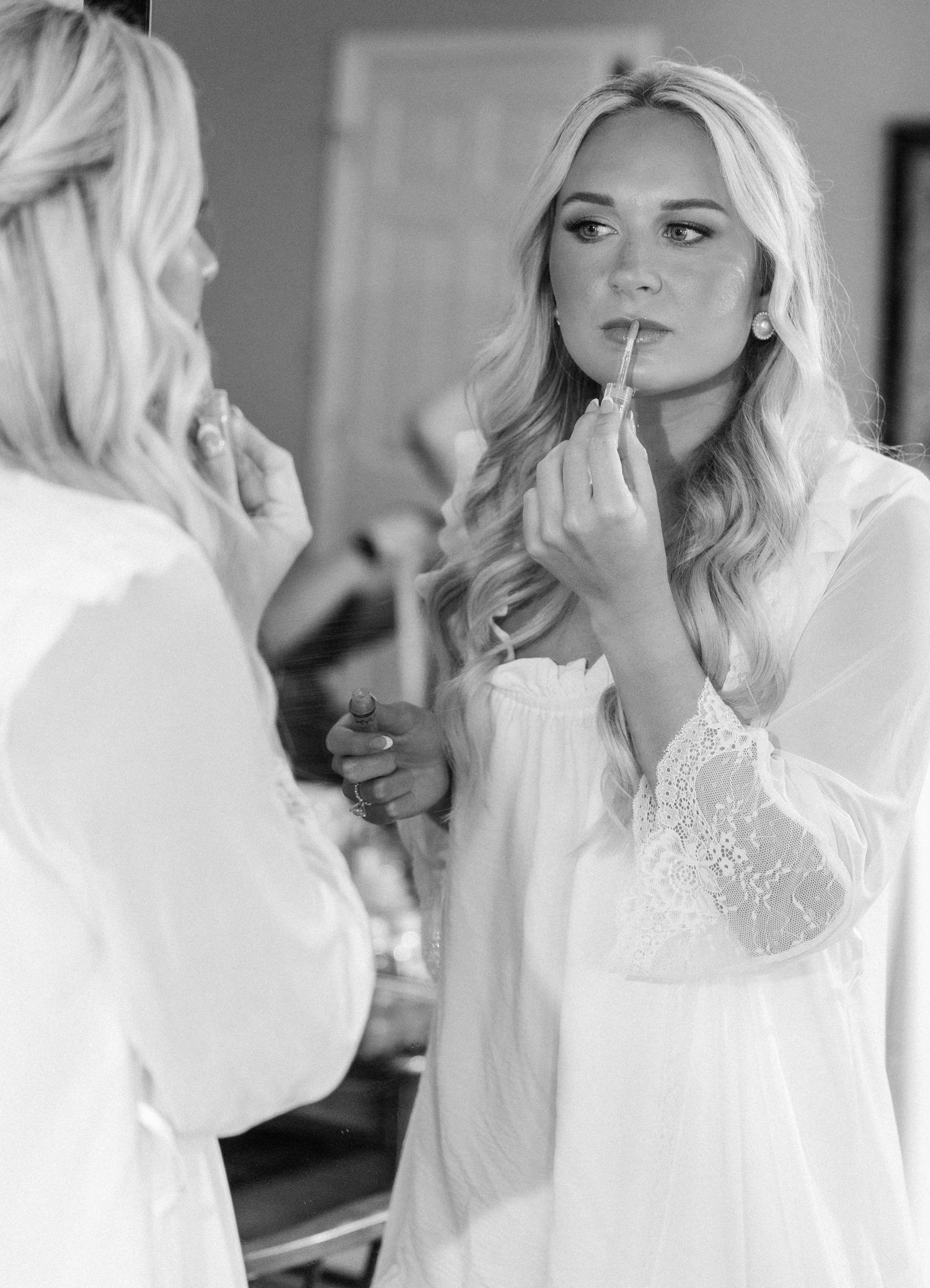 Black and white photo of blonde bride applying lipstick while getting ready for wedding.