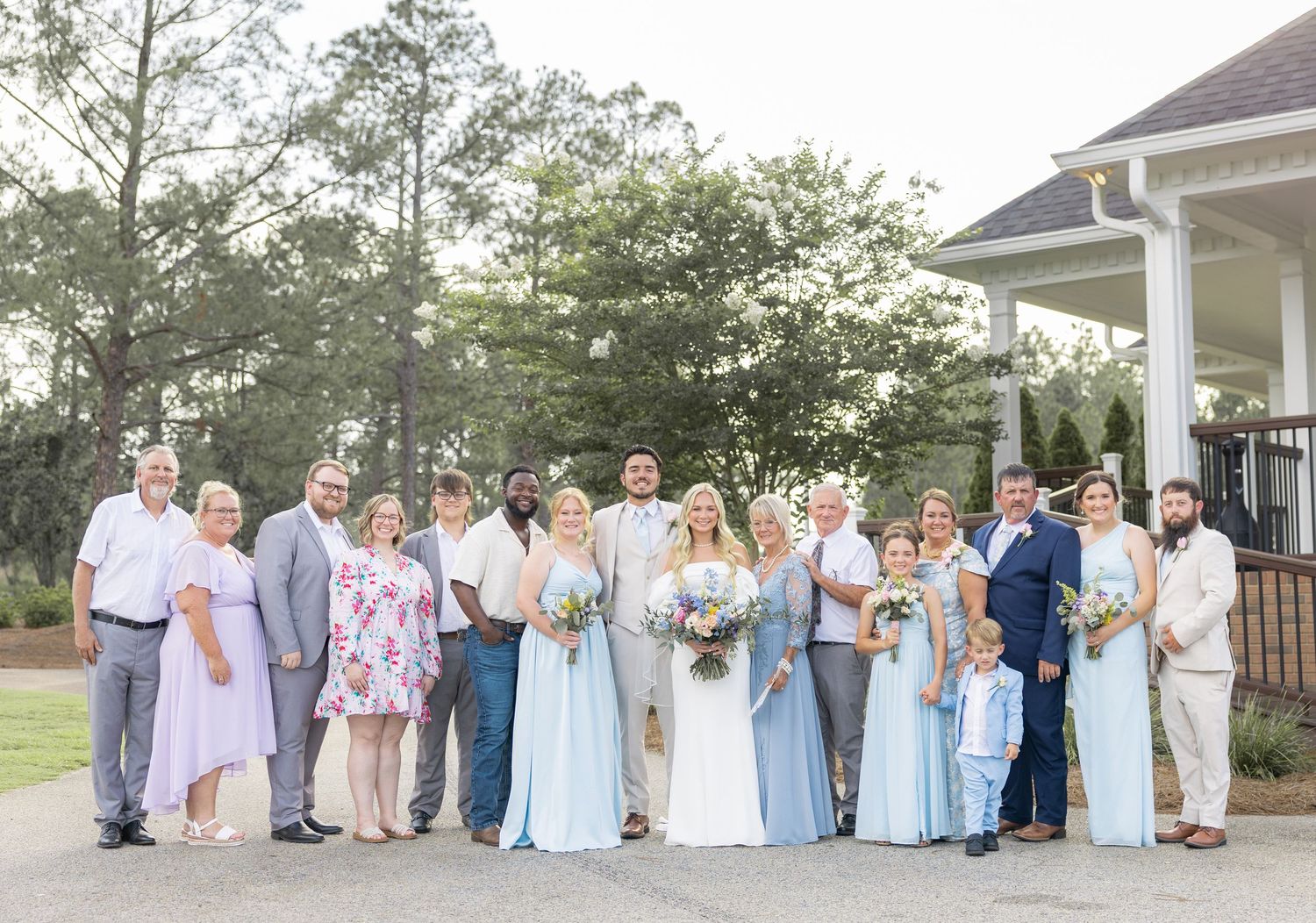 Large wedding party group photo outdoors with bridesmaids in light blue dresses and lush greenery.