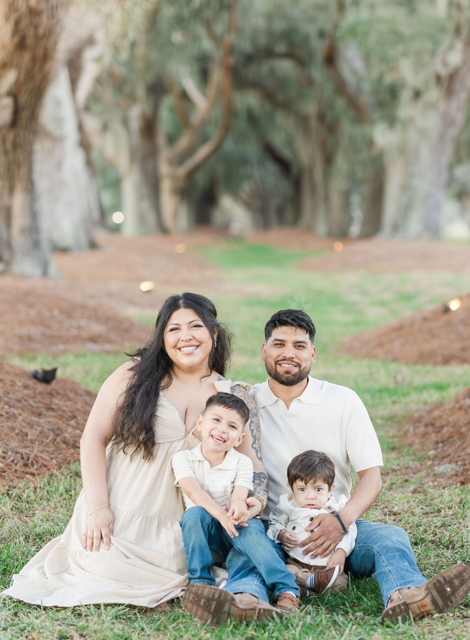 A family relaxes together on fallen pine needles in a peaceful wooded setting during an outdoor photo session.