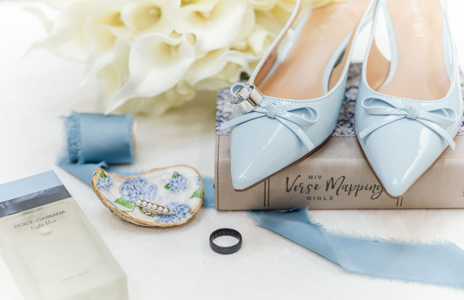Light blue wedding shoes and delicate bridal accessories arranged on white linen background.