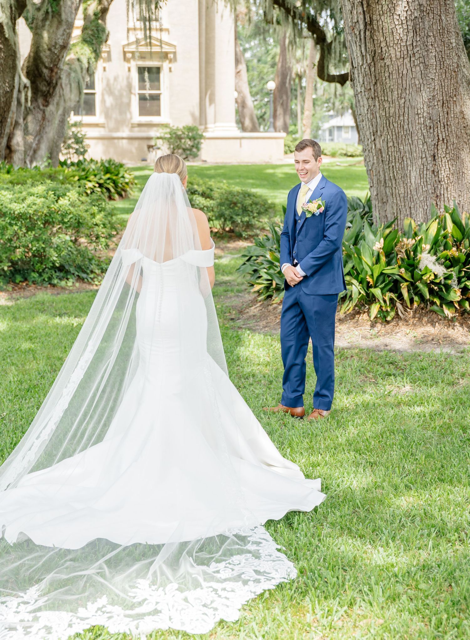 A couple shares an intimate first look moment in a garden setting with a flowing white wedding dress and navy suit.
