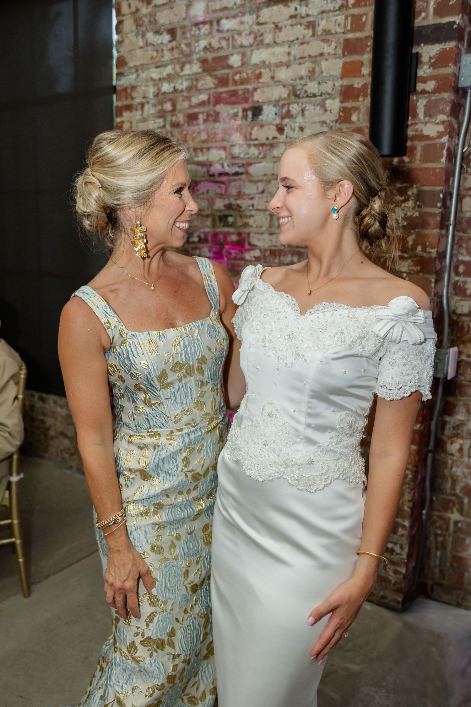 Two guests sharing a joyful moment at a wedding reception in front of exposed brick walls.
